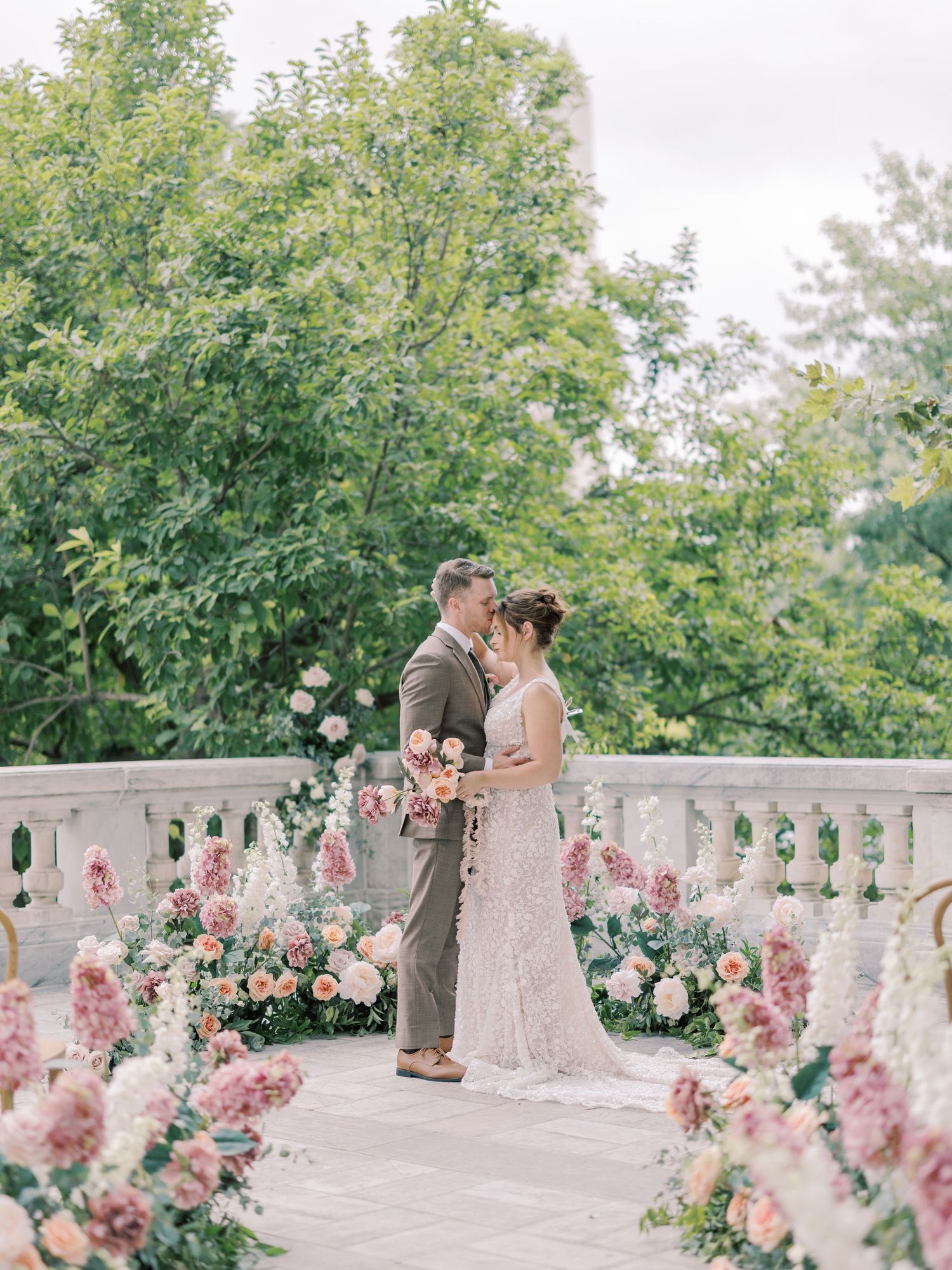 Couple shares intimate moment on balcony decorated with pink floral arrangements.