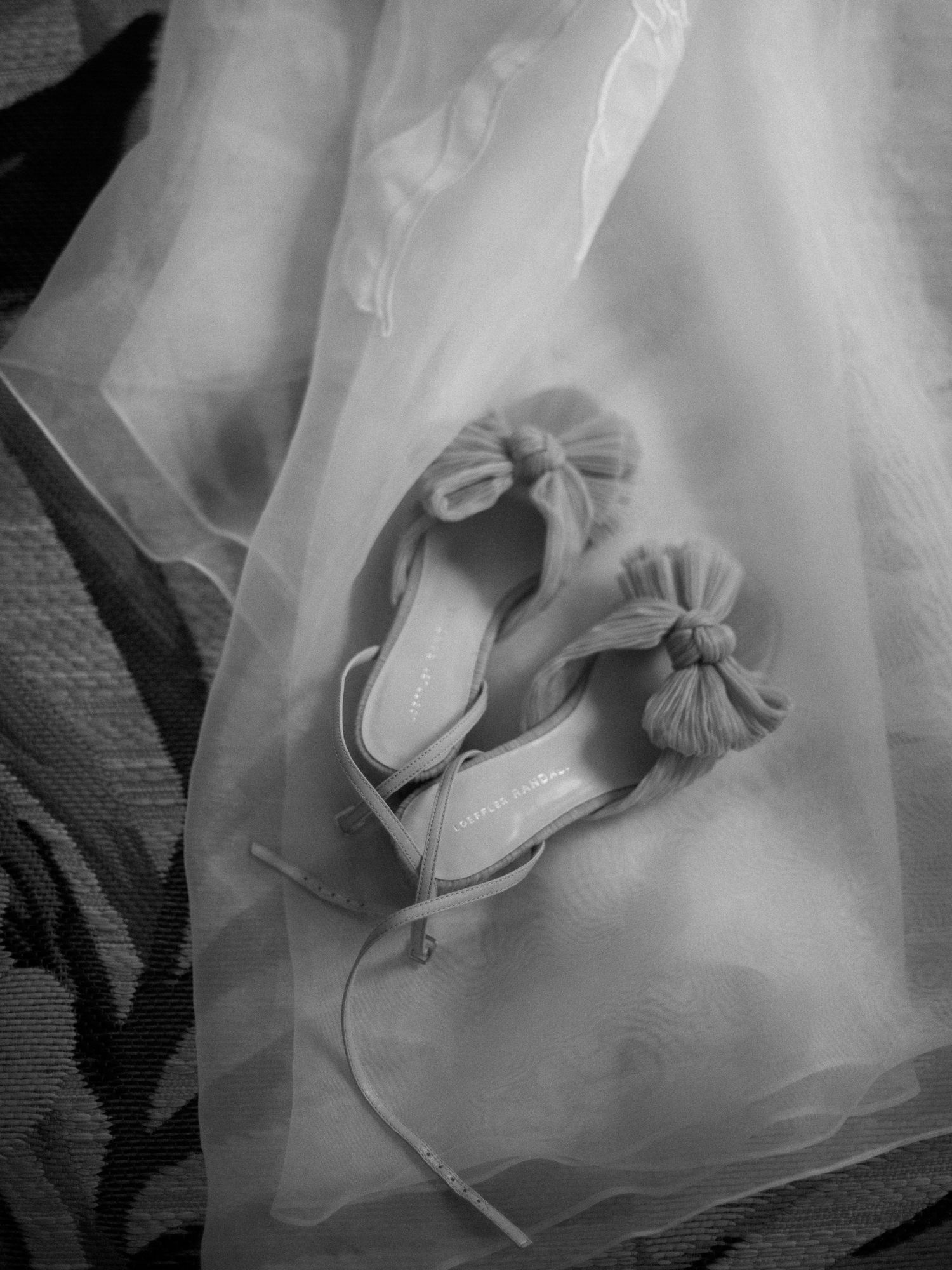 Black and white image of elegant bridal shoes with bow details on tulle fabric.