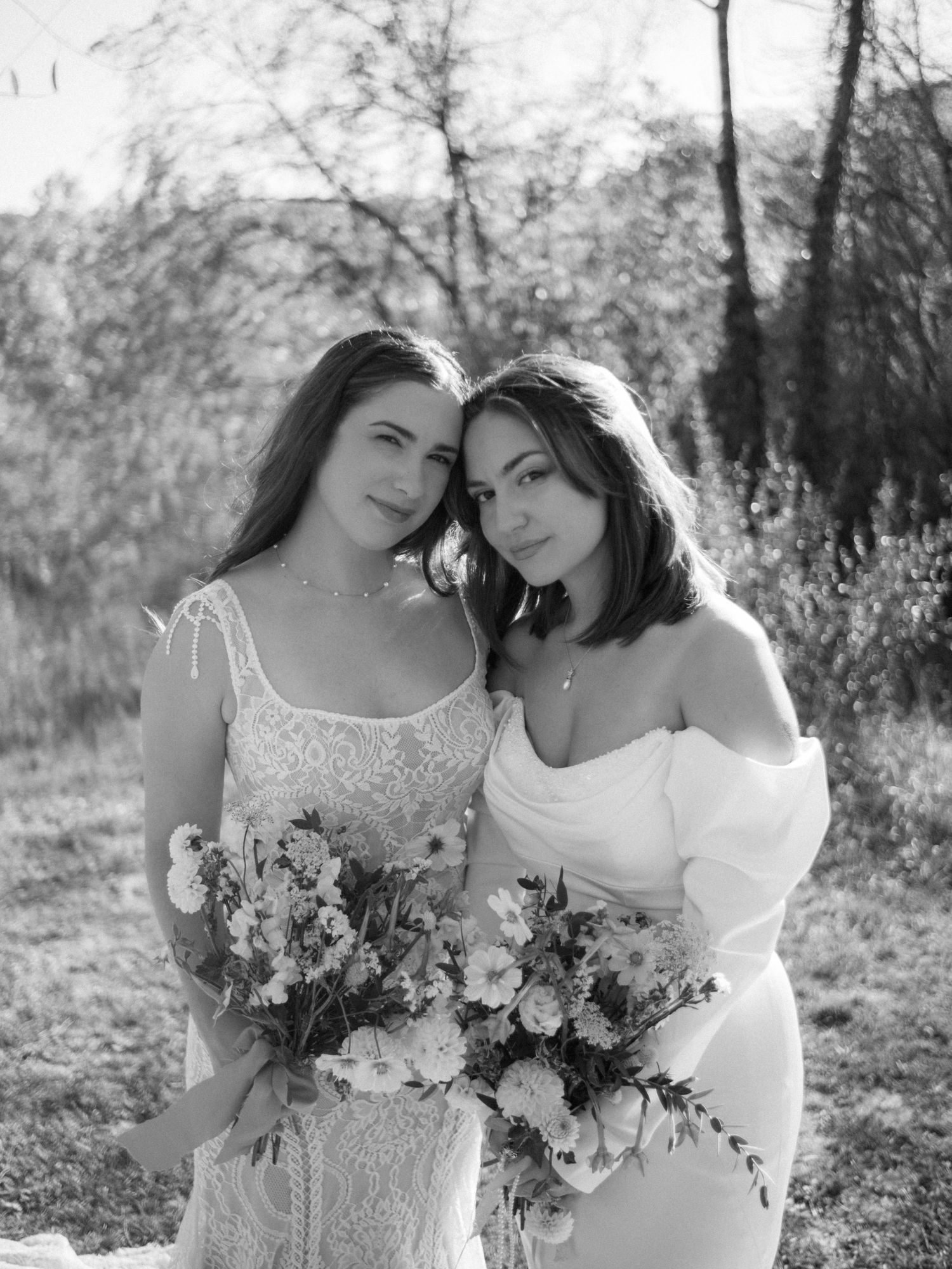 Intimate black and white portrait of two brides holding floral bouquets outdoors.