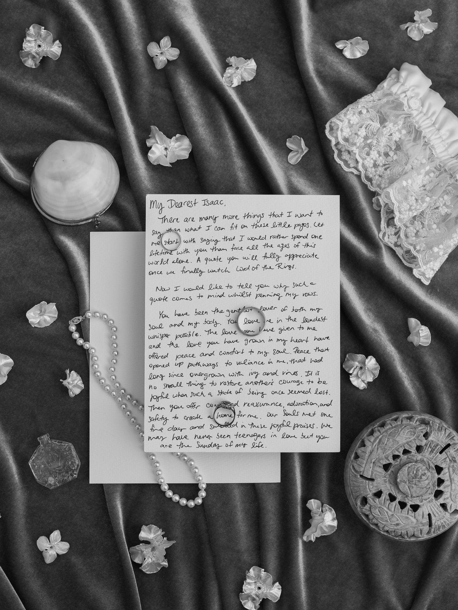 Wedding rings and handwritten note displayed on dark silk with scattered flower petals.