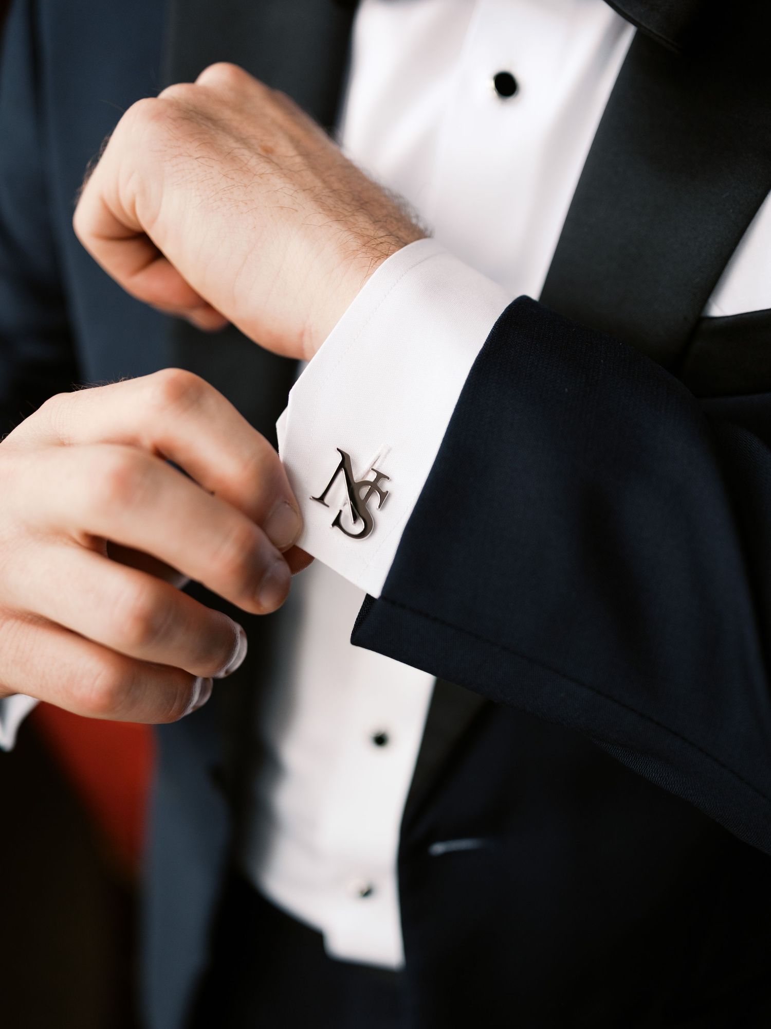 Close-up of monogrammed cufflink on formal tuxedo shirt sleeve.