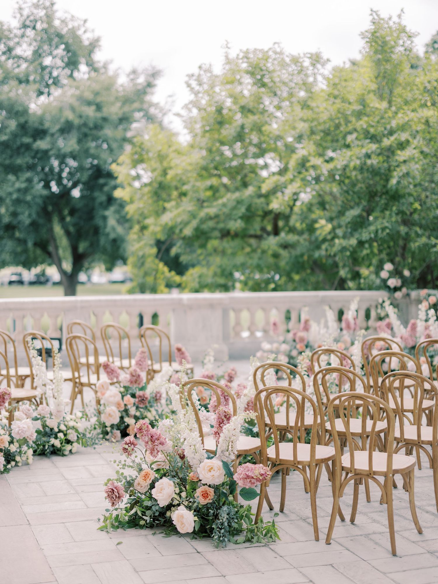 Elegant outdoor wedding ceremony setup with wooden chairs and pink floral aisle decorations.
