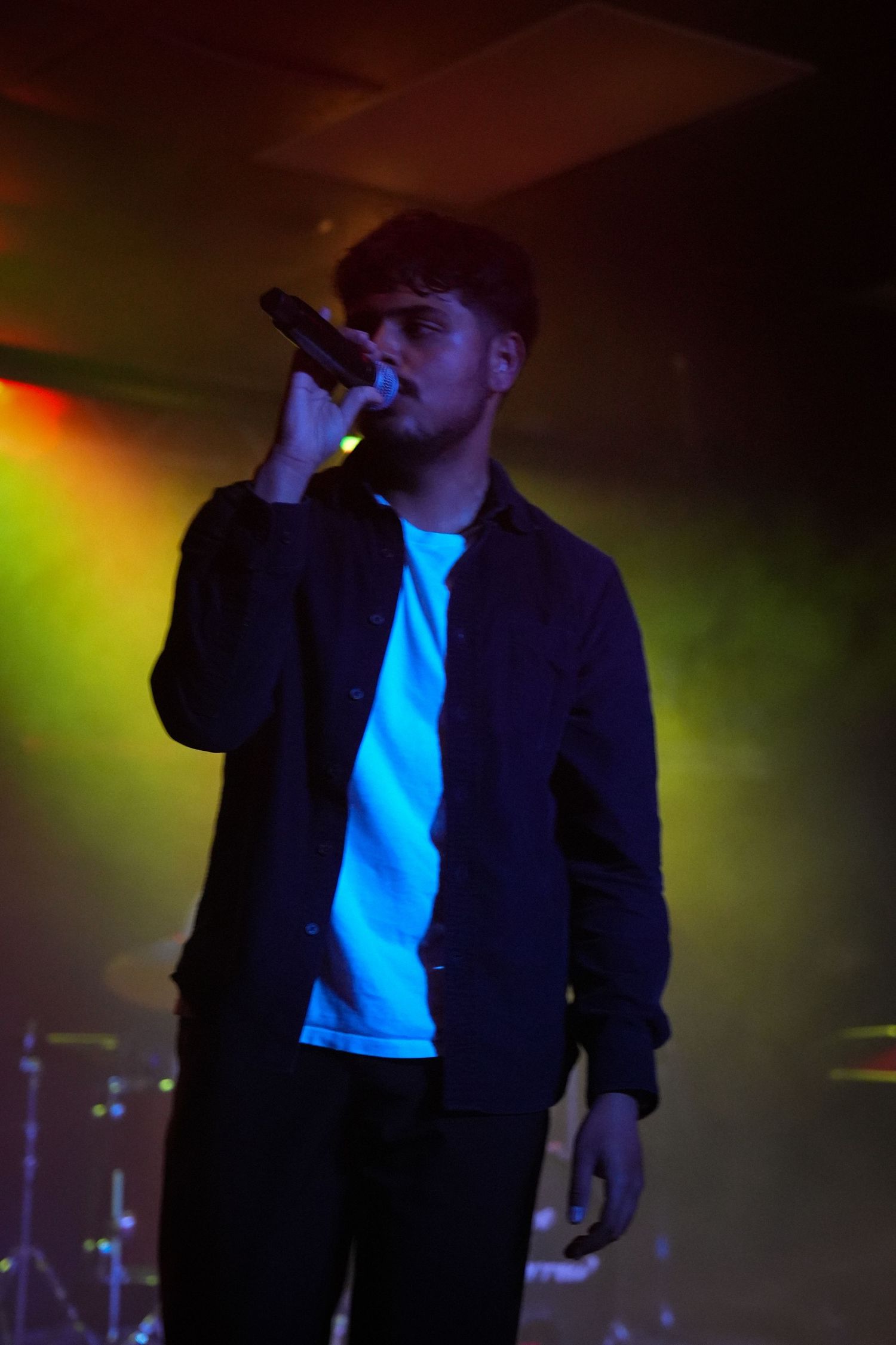 Male vocalist performing on stage under colorful blue and orange stage lighting with microphone.