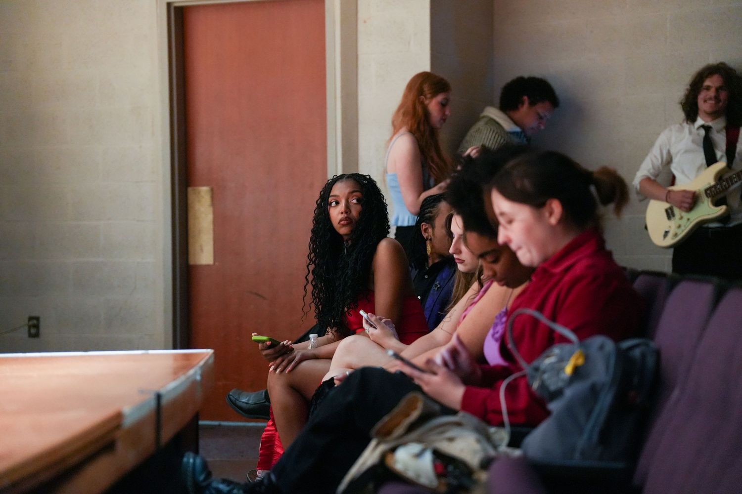 Students sit in a room with purple chairs while a guitarist performs in the background.