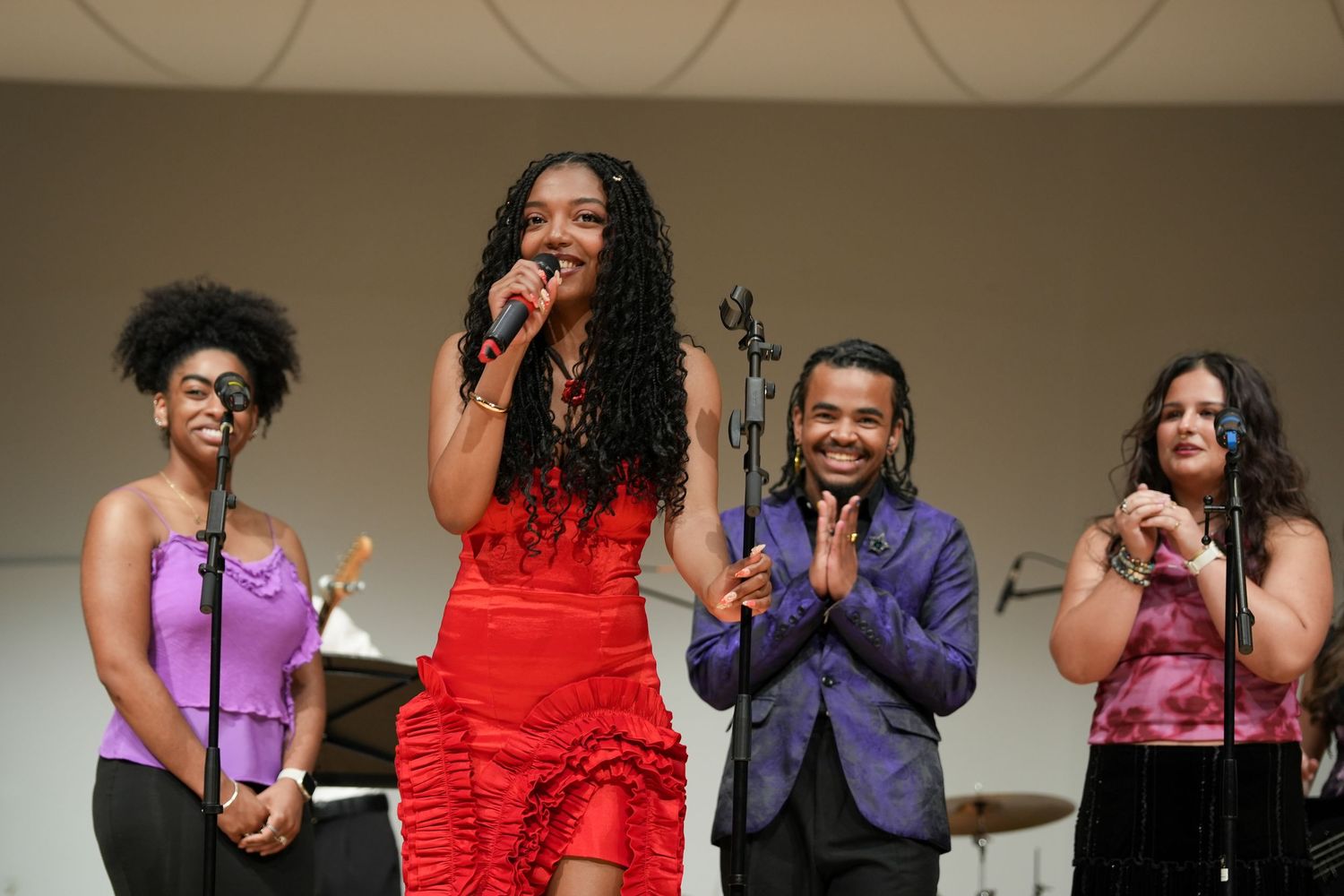 Four performers on stage, with a woman in red dress holding microphone flanked by three backup singers.