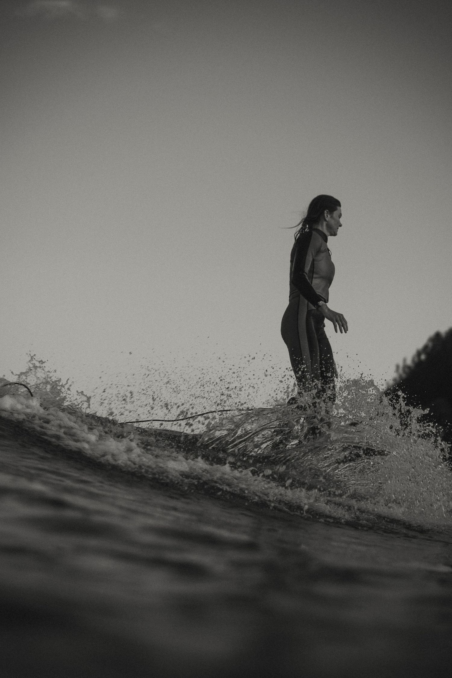 Surfer riding wave with water spray in dramatic black and white composition.
