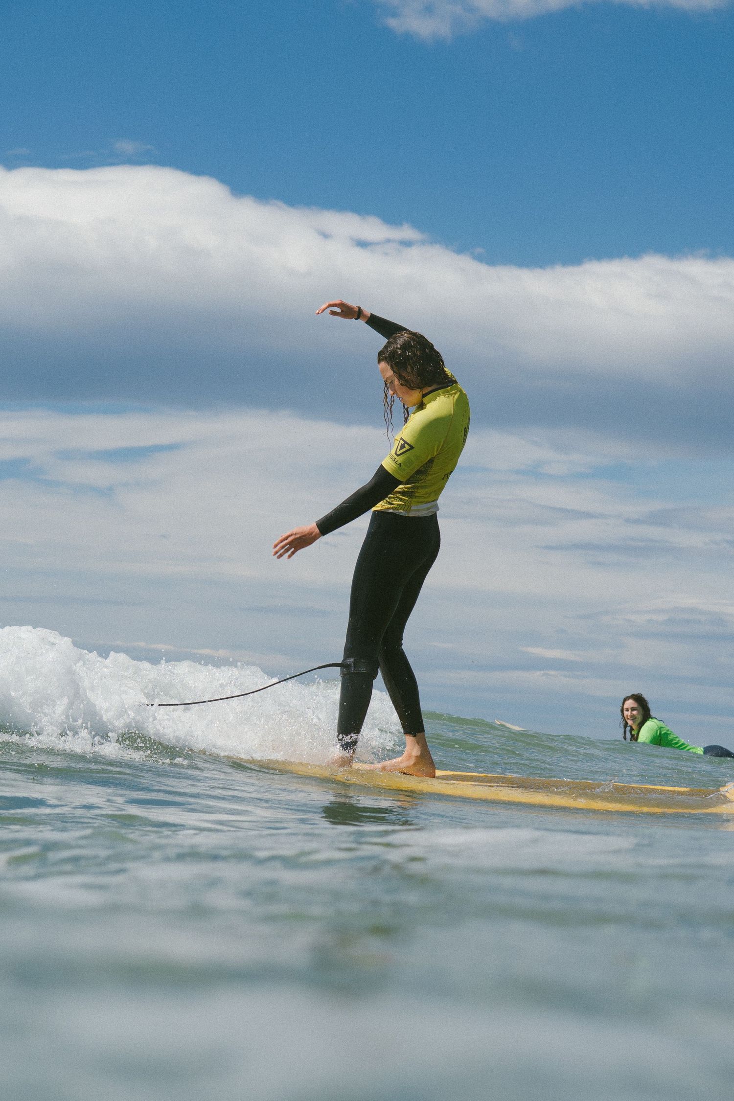 Surfer practicing balance moves on yellow longboard in gentle ocean waves.