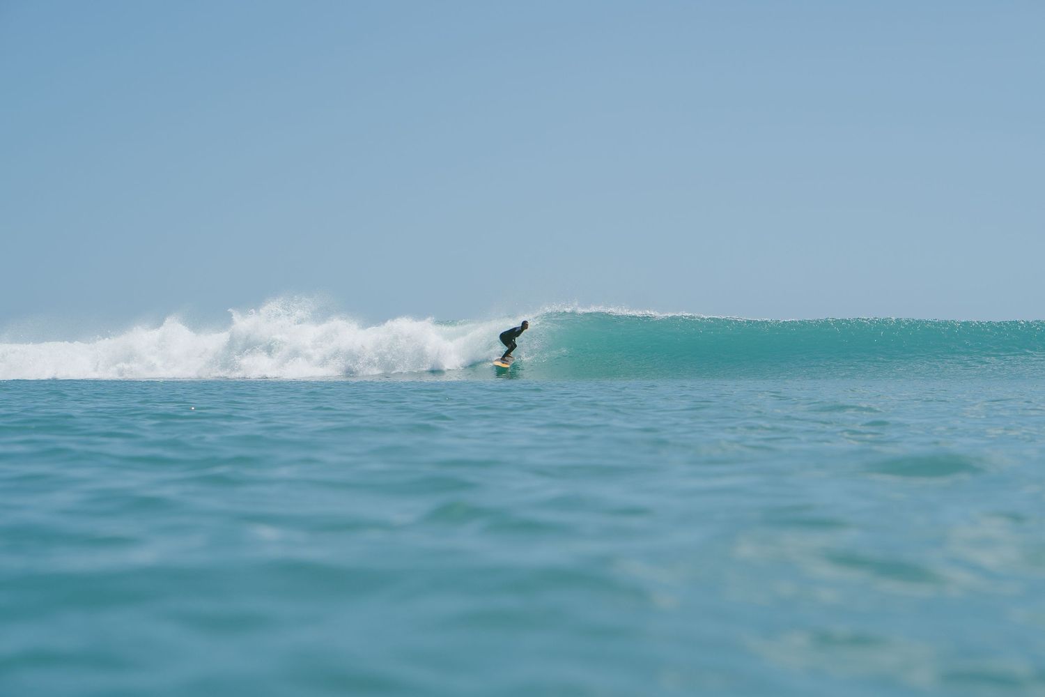Distant surfer catches a wave on pristine turquoise ocean waters.