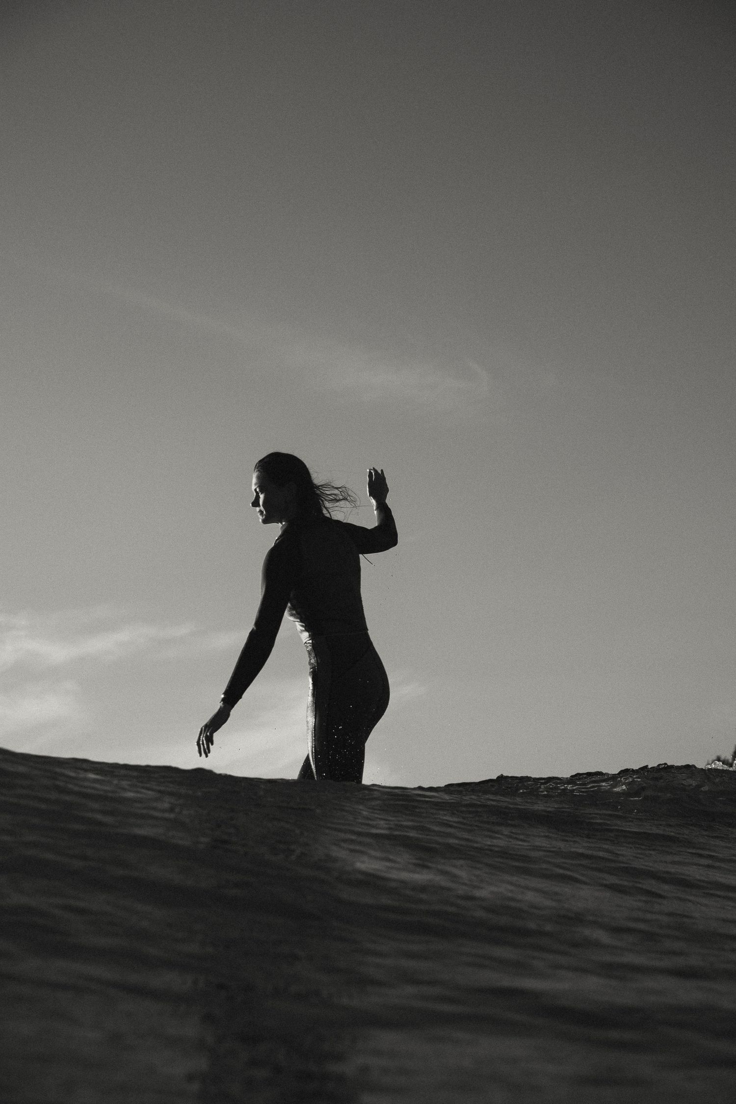 A silhouetted figure stands on a surfboard against a moody sky.