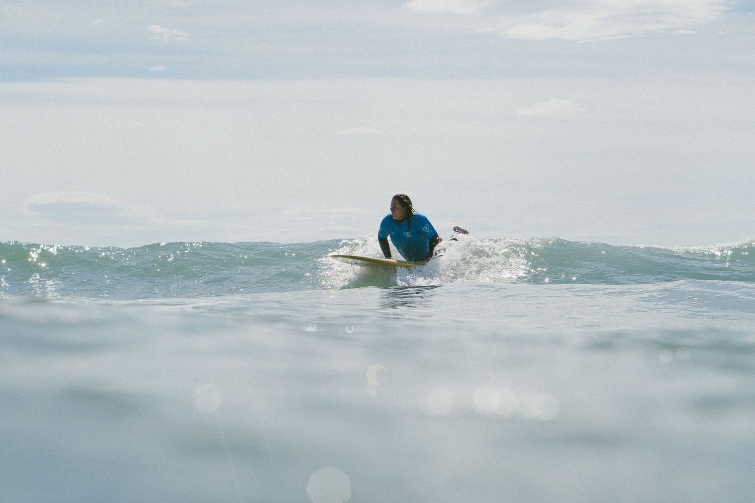 Distant view of surfer riding ocean waves against a mountainous coastal backdrop.