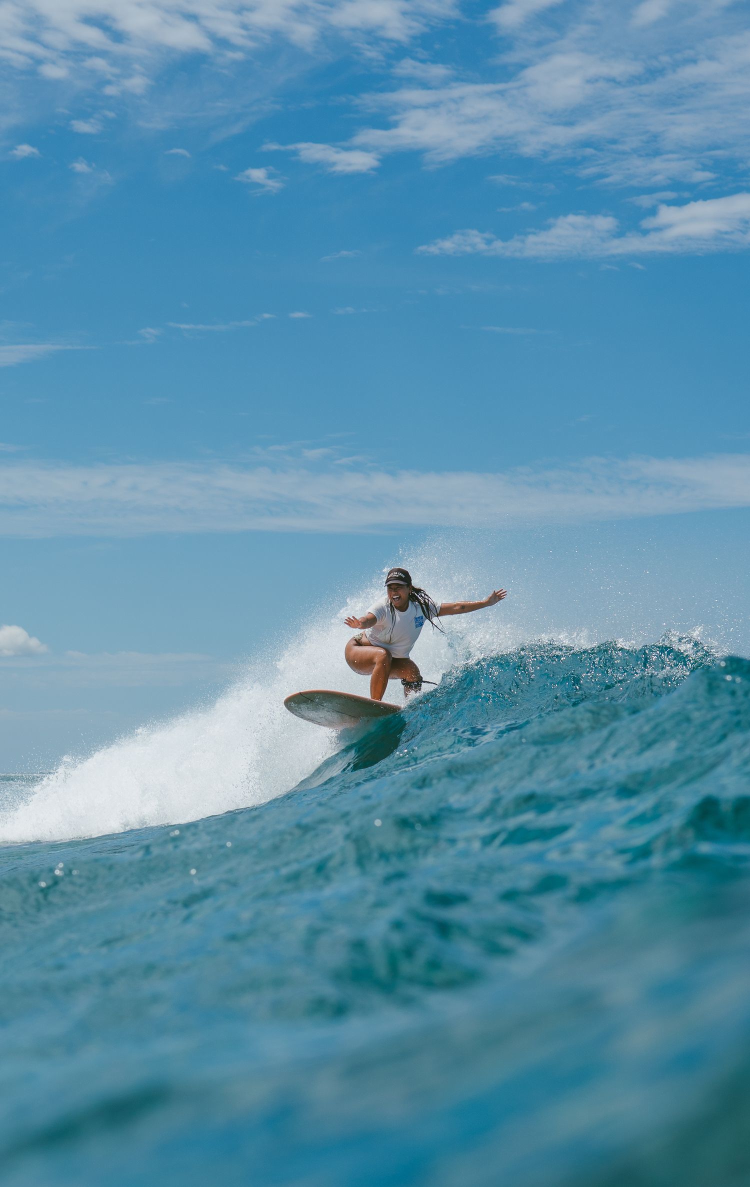 Surfer rides a large turquoise ocean wave under bright blue skies.