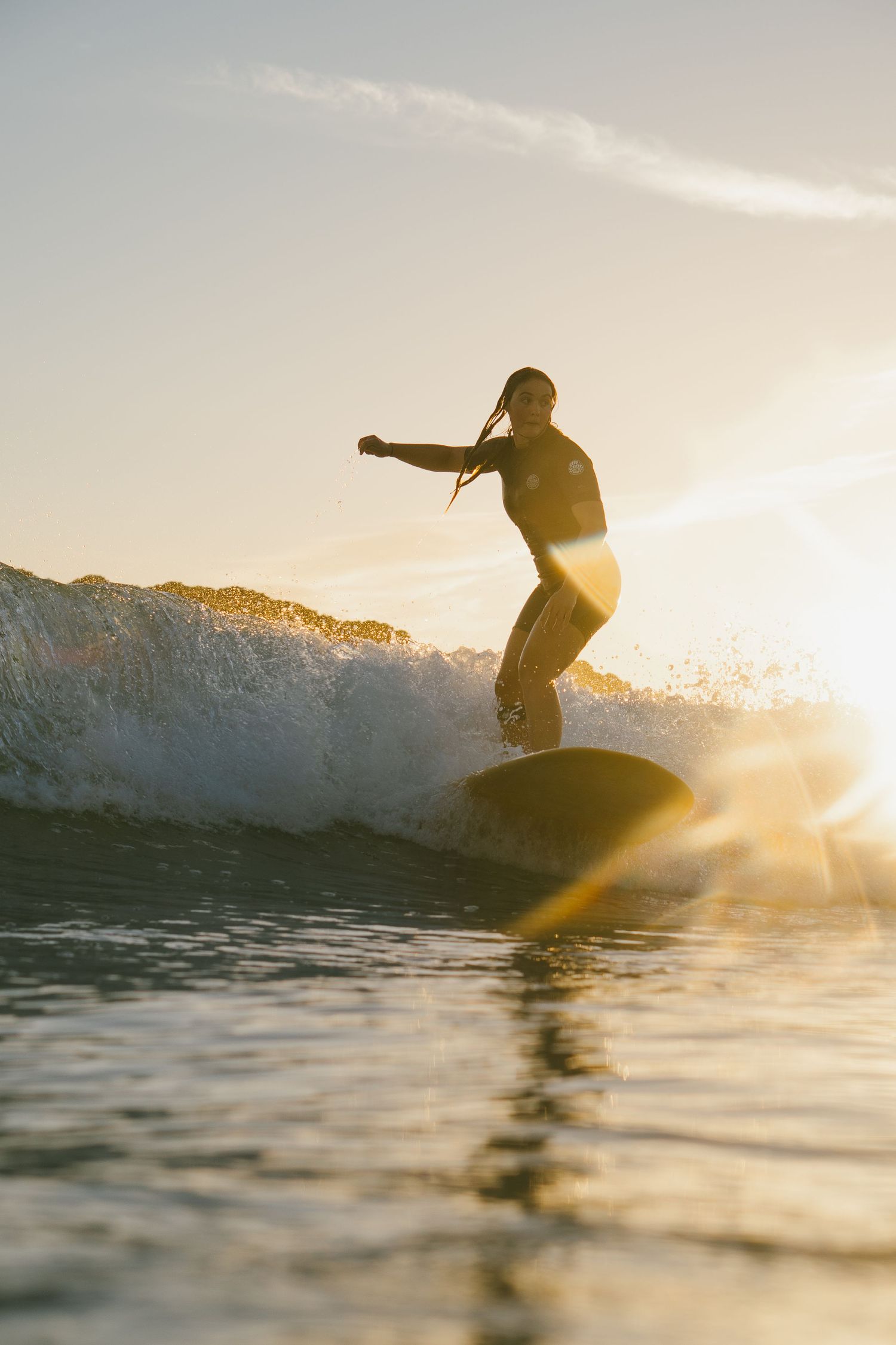 Surfer silhouette riding wave during golden hour with sun rays breaking through.