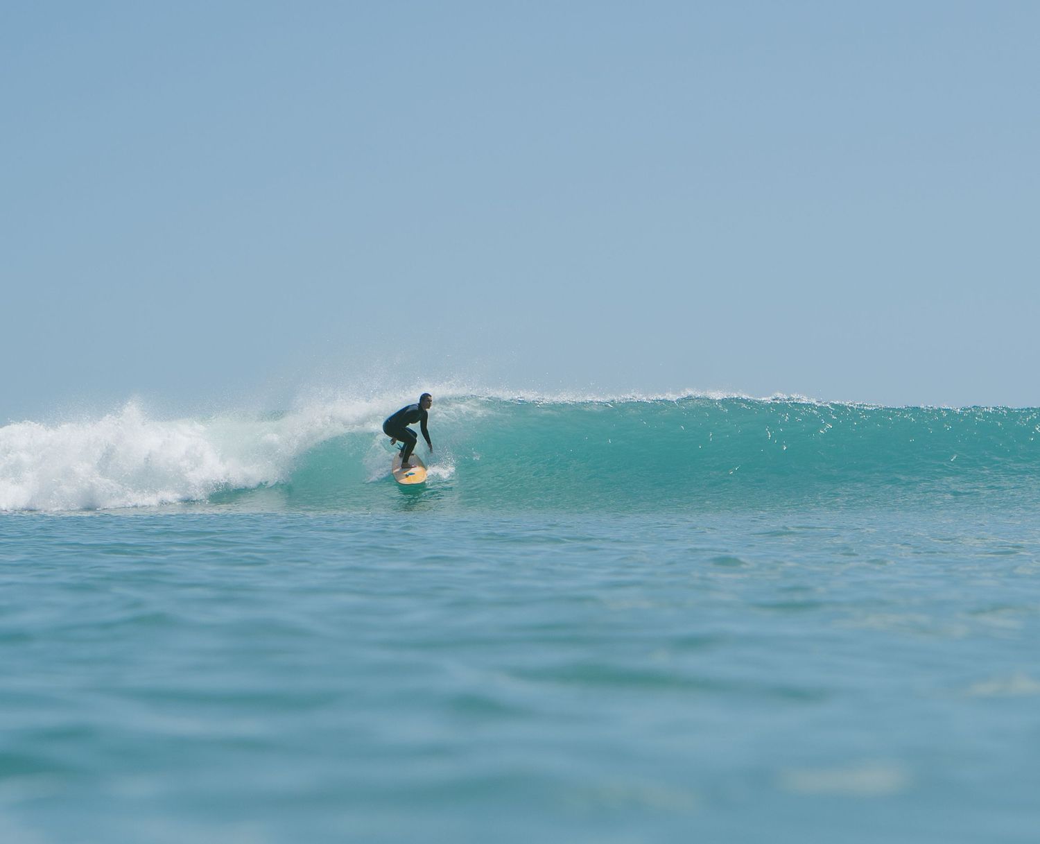 Surfer glides down a turquoise wave face on a bright sunny day.