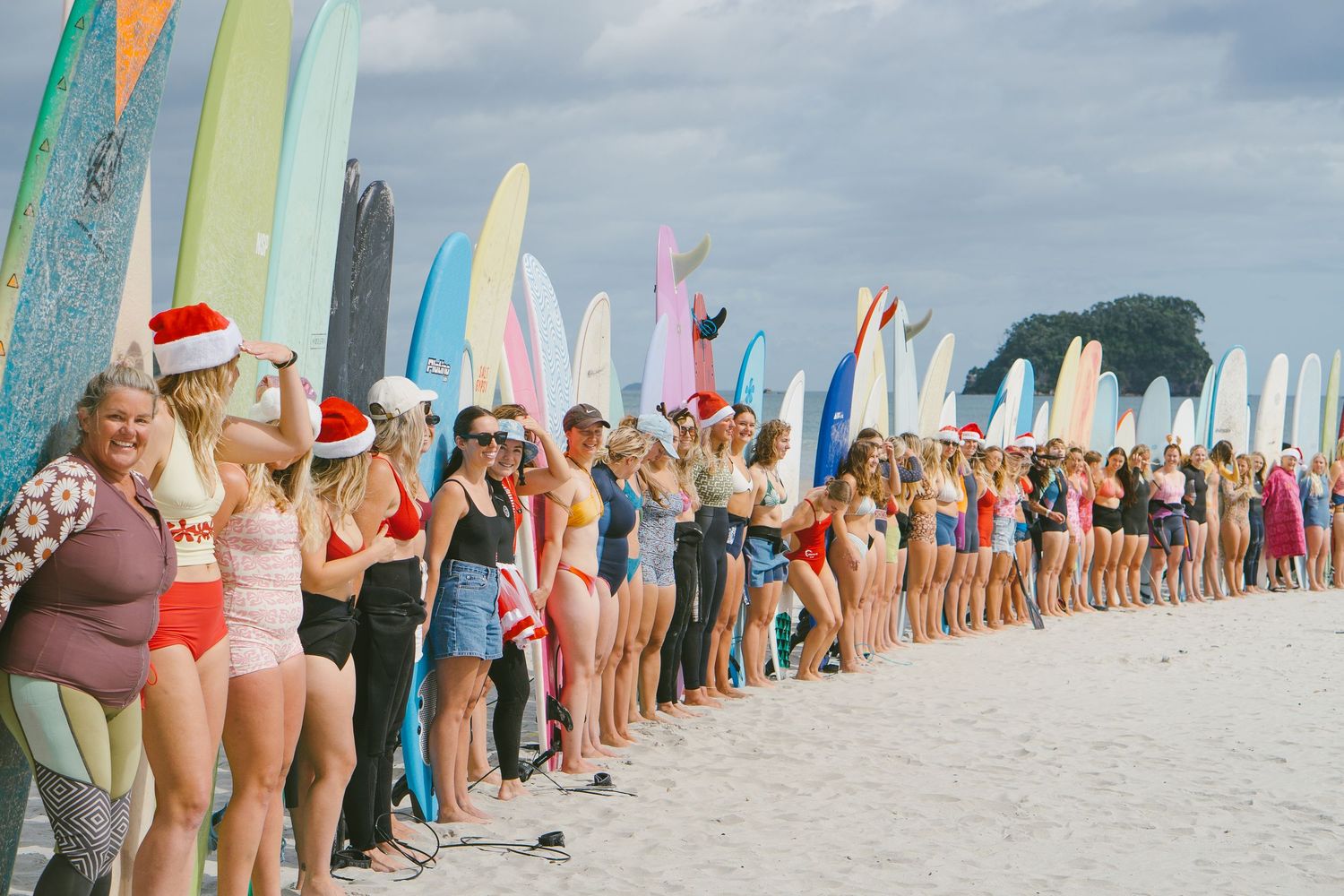 Large group of surfers lined up on beach with colorful surfboards during beach event.