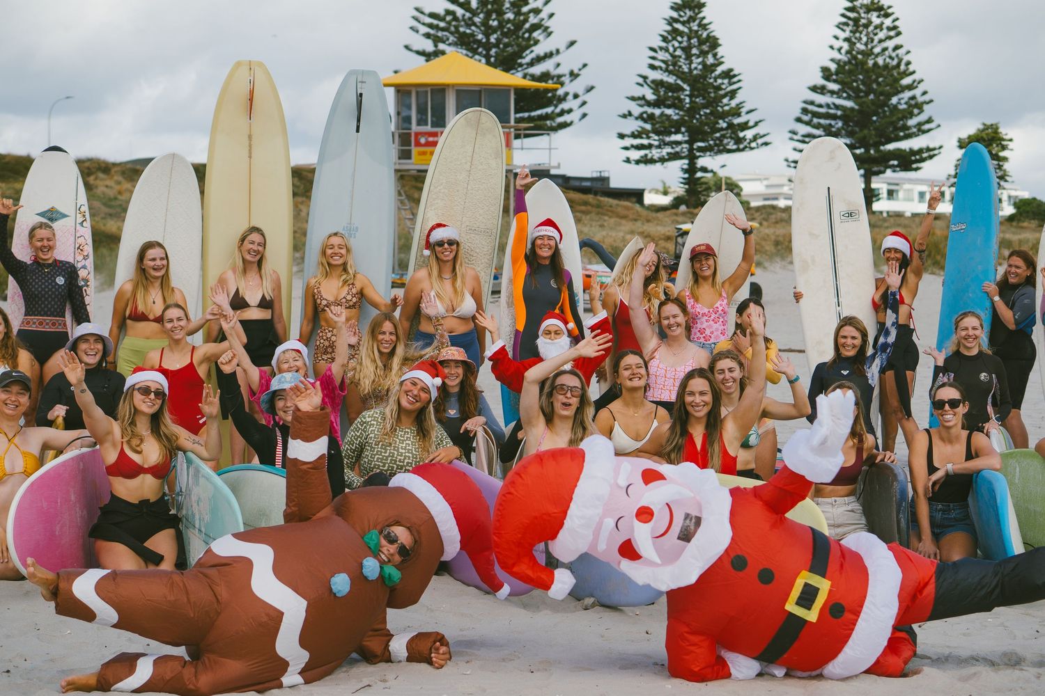 Large group of surfers celebrating on a beach with surfboards and festive holiday attire.