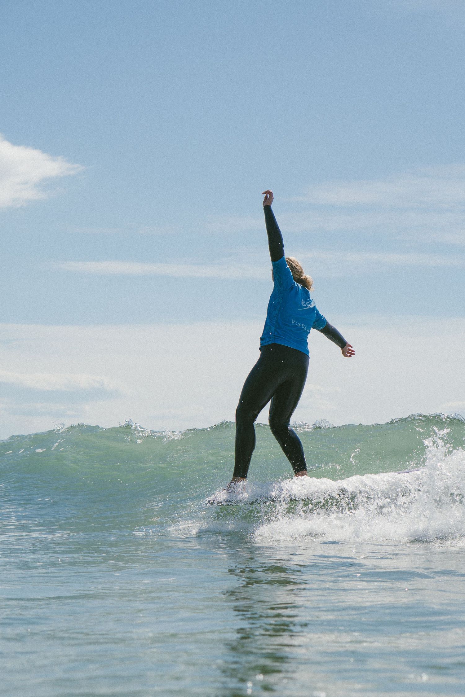 Surfer in blue jacket performs stylish maneuver on breaking wave.
