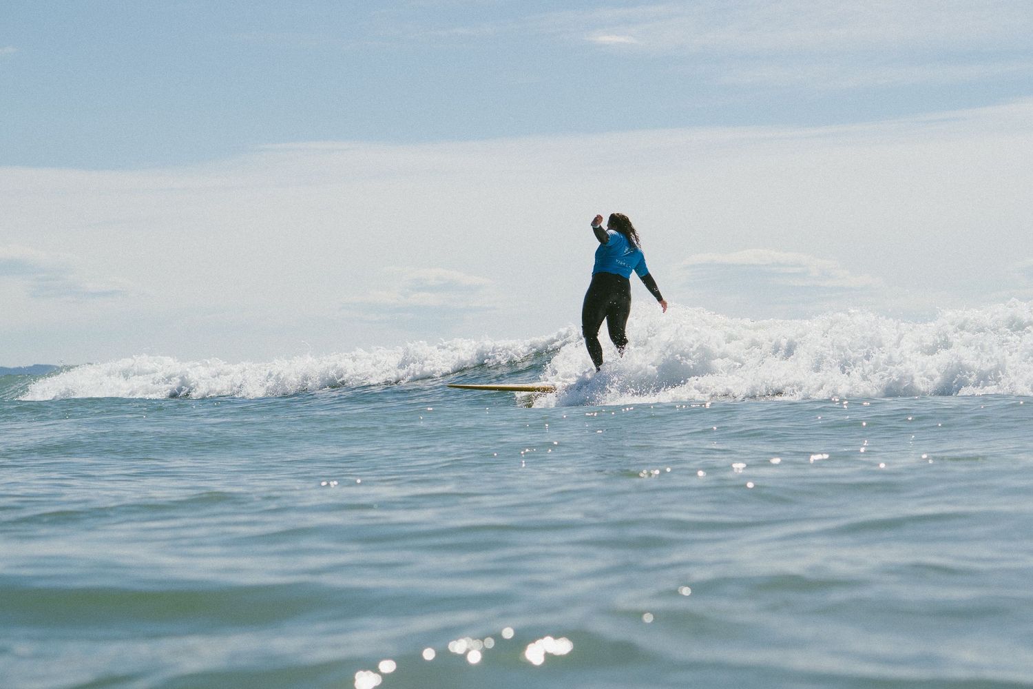 Surfer glides across rolling waves on a bright day with mountains in the background.