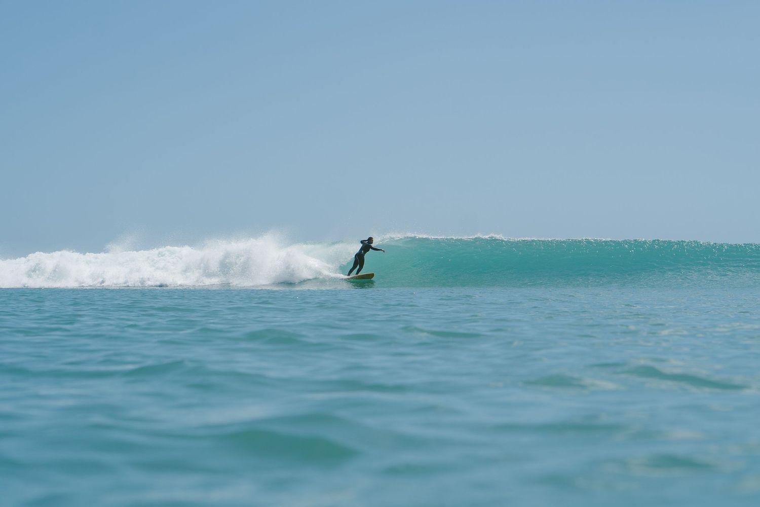 Surfer navigates a breaking wave in crystal clear tropical waters.