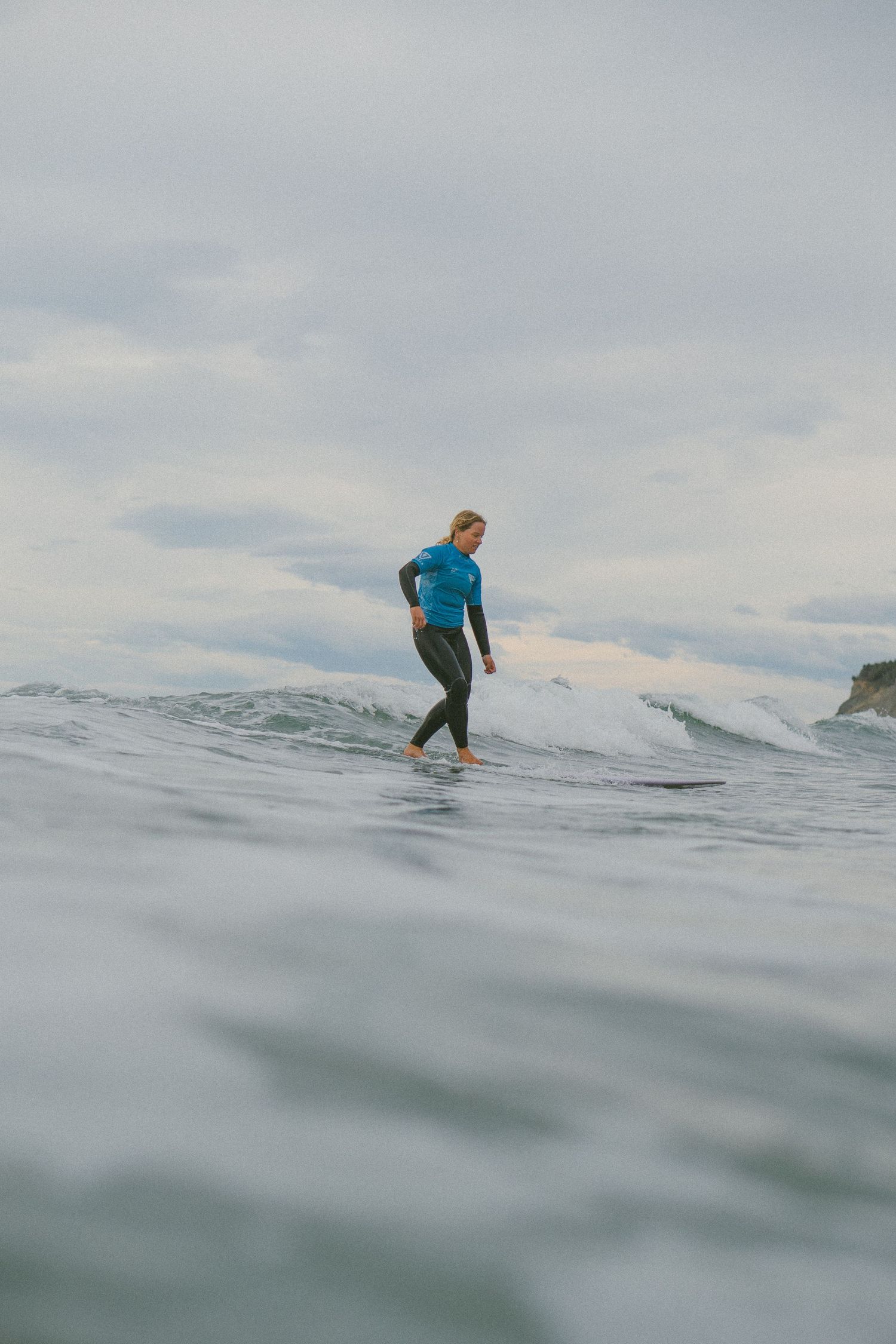 Surfer riding waves on a cloudy day with water splashing around.
