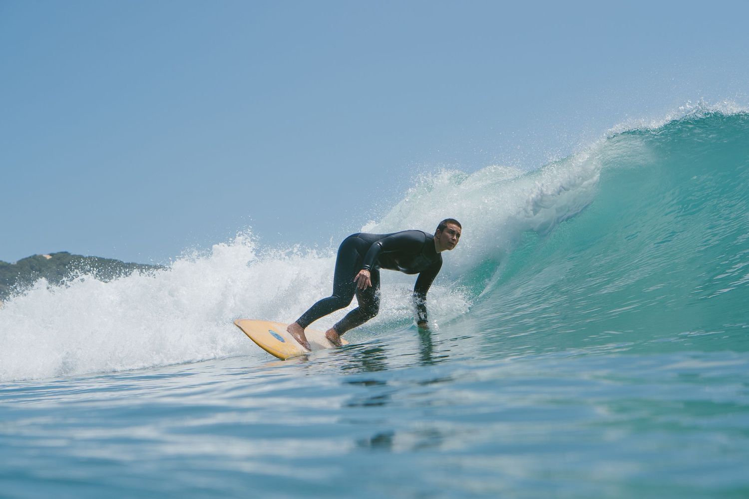 Surfer rides low on a glassy turquoise wave during a perfect session.