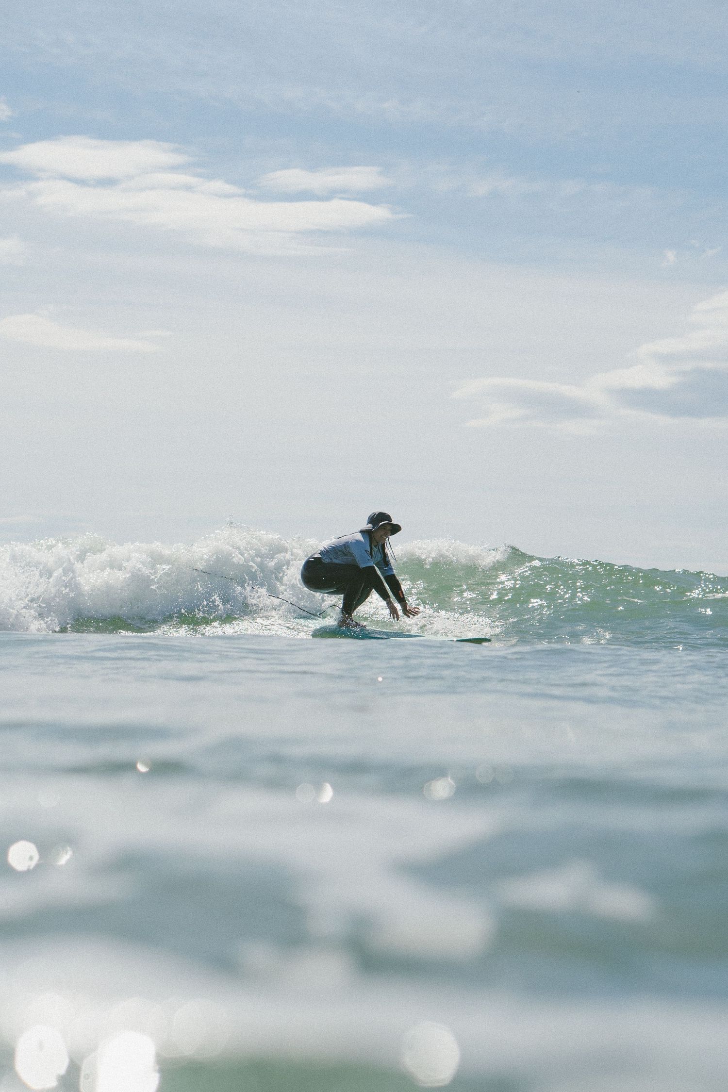 Surfer navigating through breaking waves on a light blue ocean under cloudy skies.