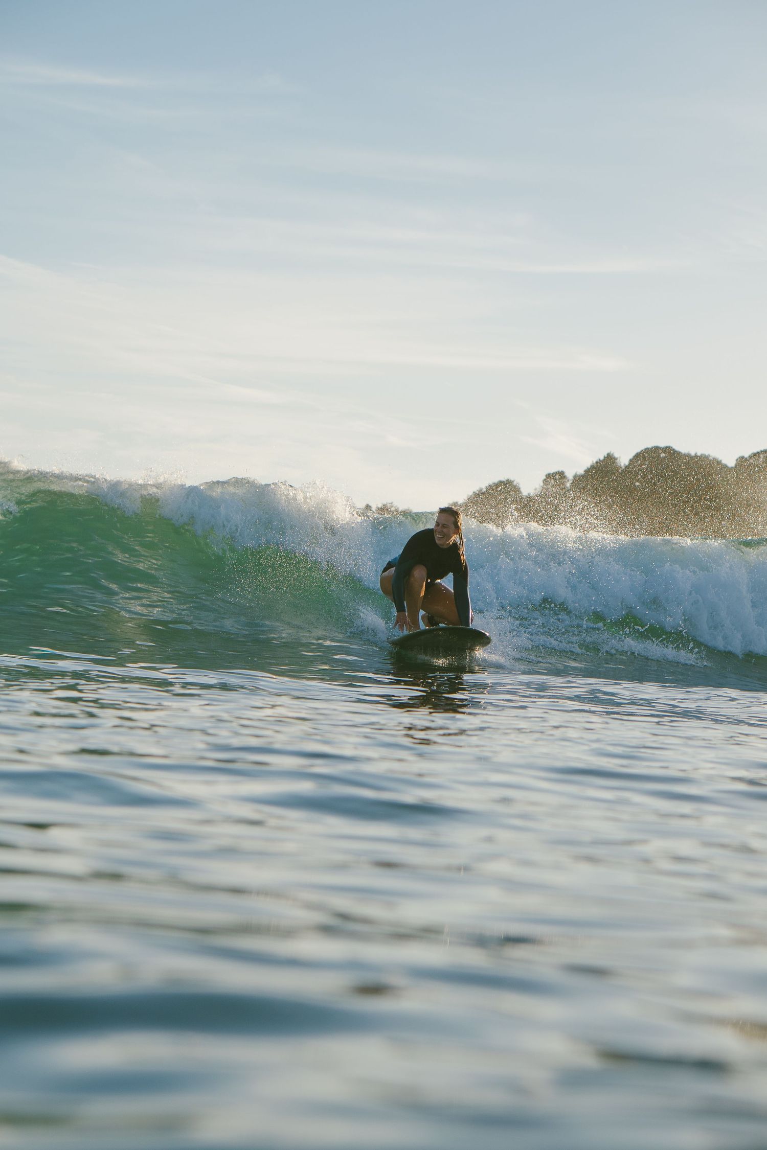 Surfer catching a turquoise wave with rocky coastline in background.