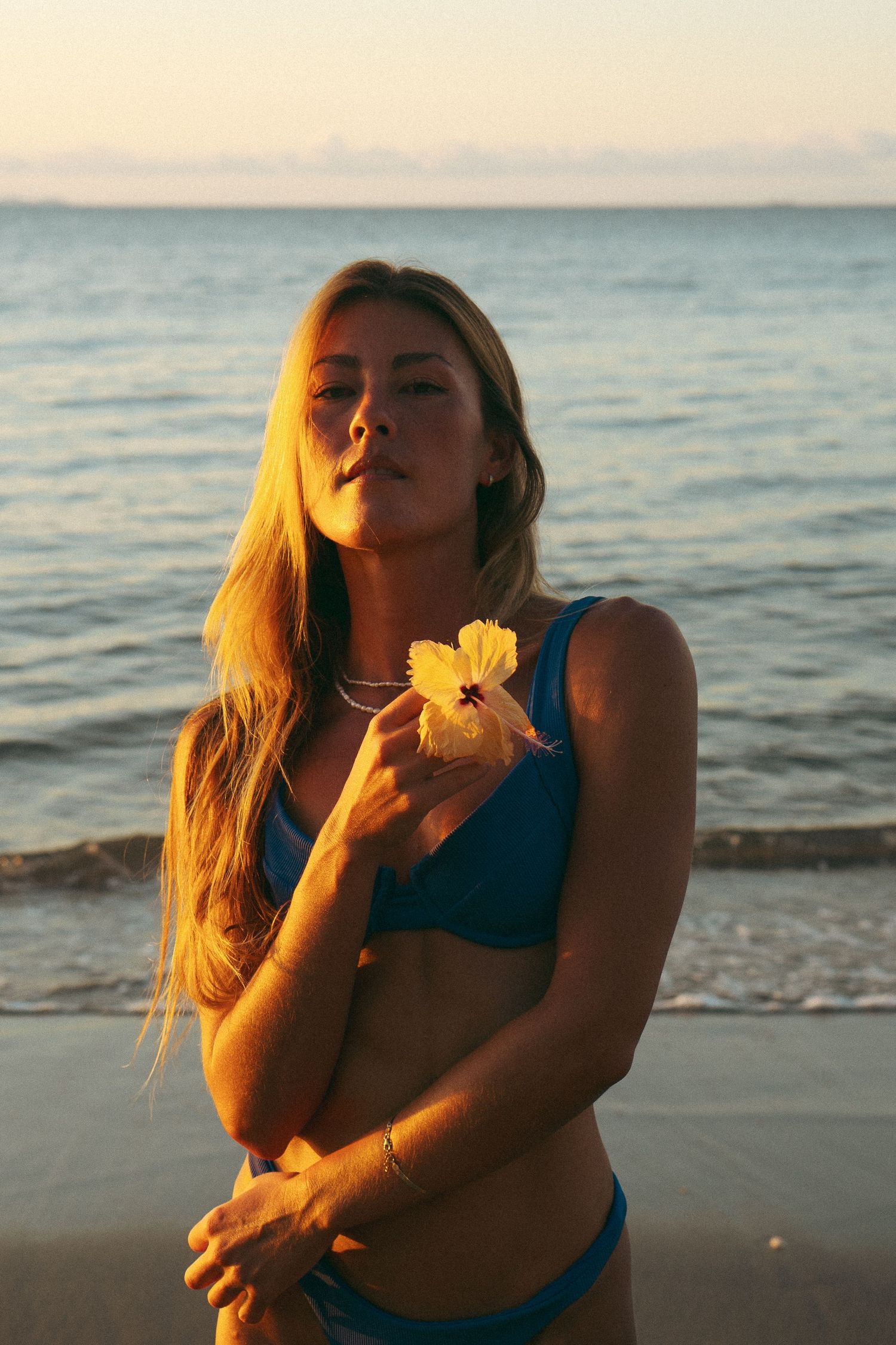 Person in blue swimwear enjoys golden hour on a beach with ocean waves in the background.