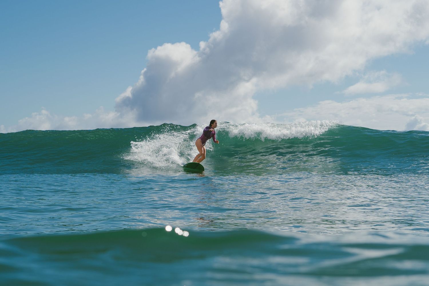 Surfer carves through rolling ocean waves on a bright sunny day.