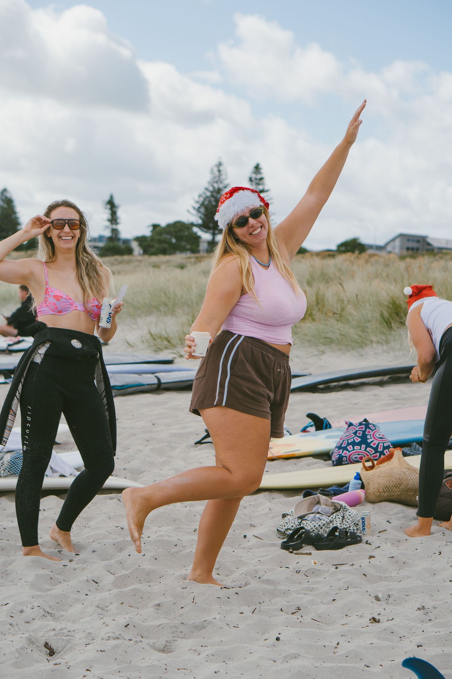 Group performs beach workout exercises while wearing Santa hats on sandy shore.