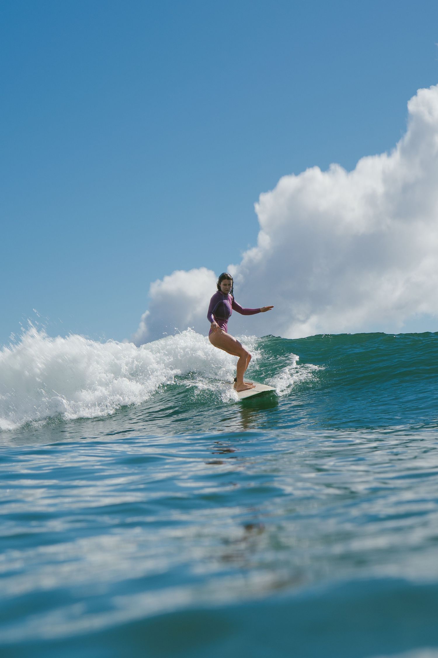 Surfer gracefully rides along the face of a turquoise ocean wave.