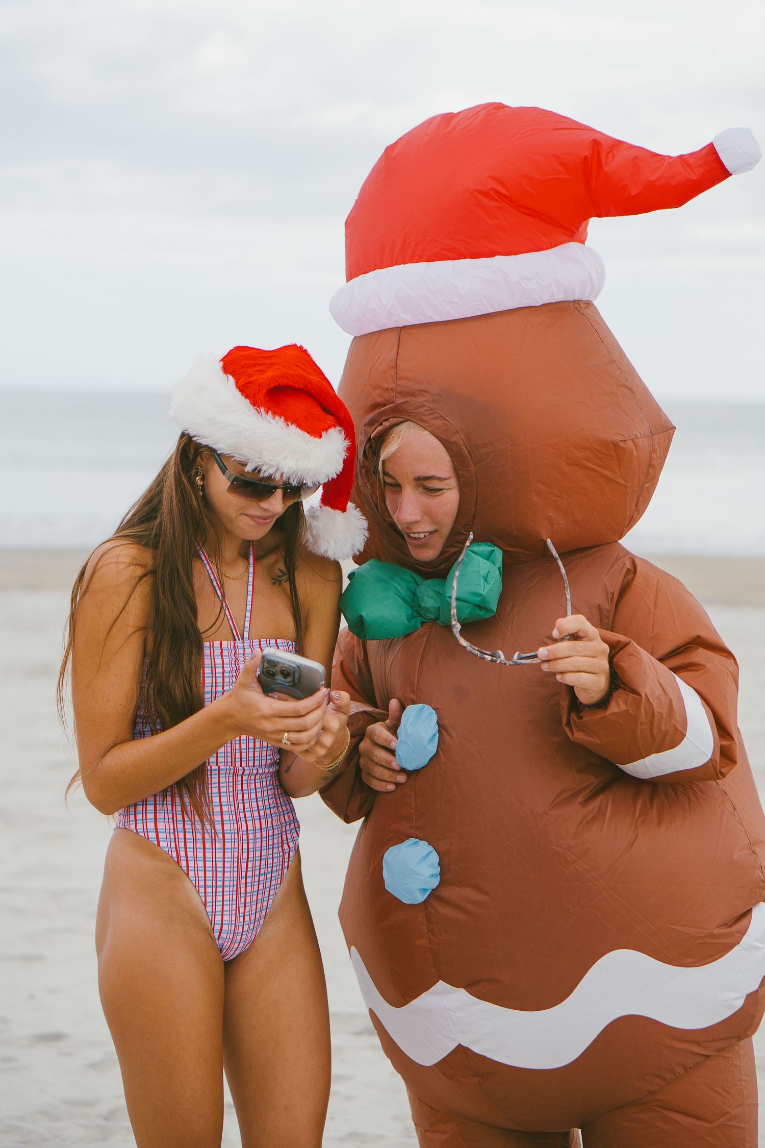 People in swimwear and Santa hats pose with someone in brown inflatable costume on beach.