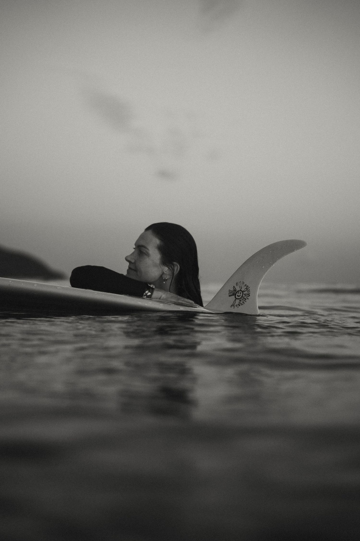 Surfer floating in calm waters with surfboard visible above surface.
