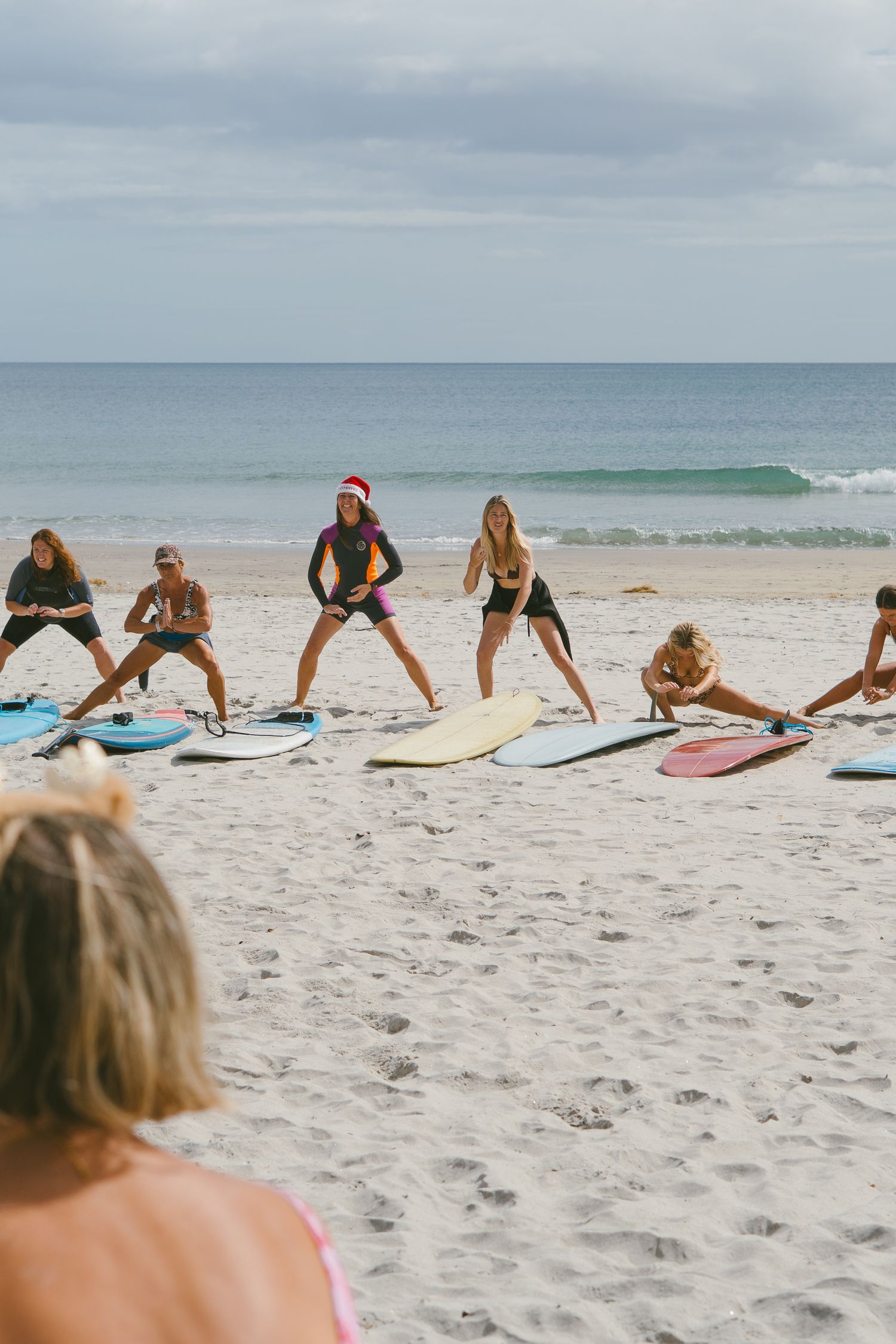 Group stretching and exercising on surfboards laid out on a sandy beach.