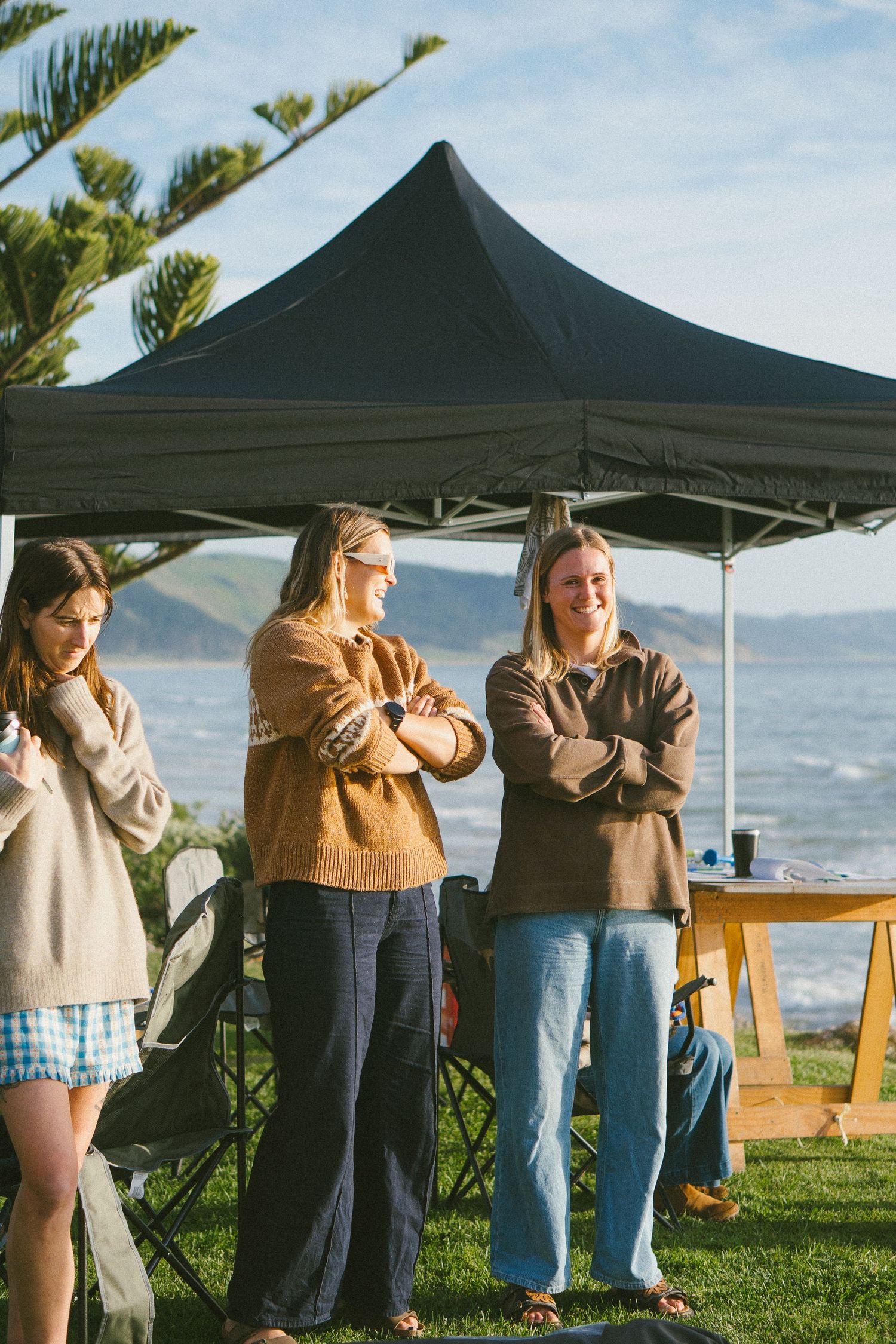 Casual outdoor gathering under black pop-up tent by the ocean.