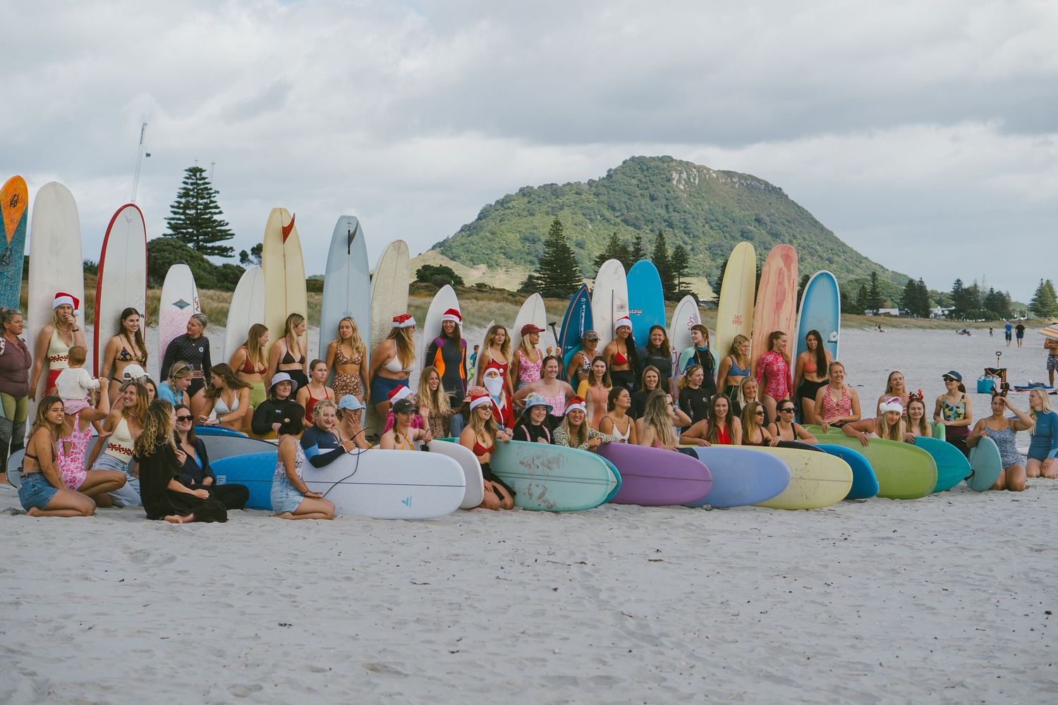 Crowd of surfers with boards gather at beach with mountain backdrop for surfing event.