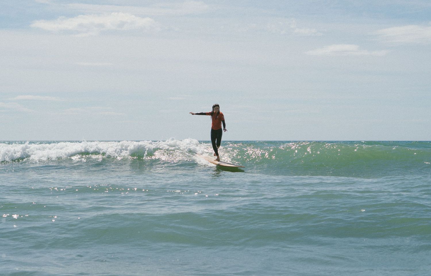 Longboard surfer rides a green wave on a clear day at the beach.