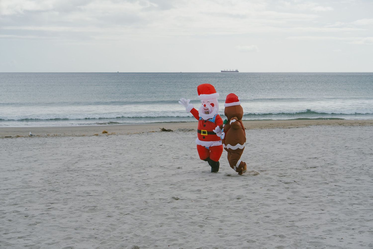 People wearing Santa hats surf in the ocean during holiday-themed beach event.