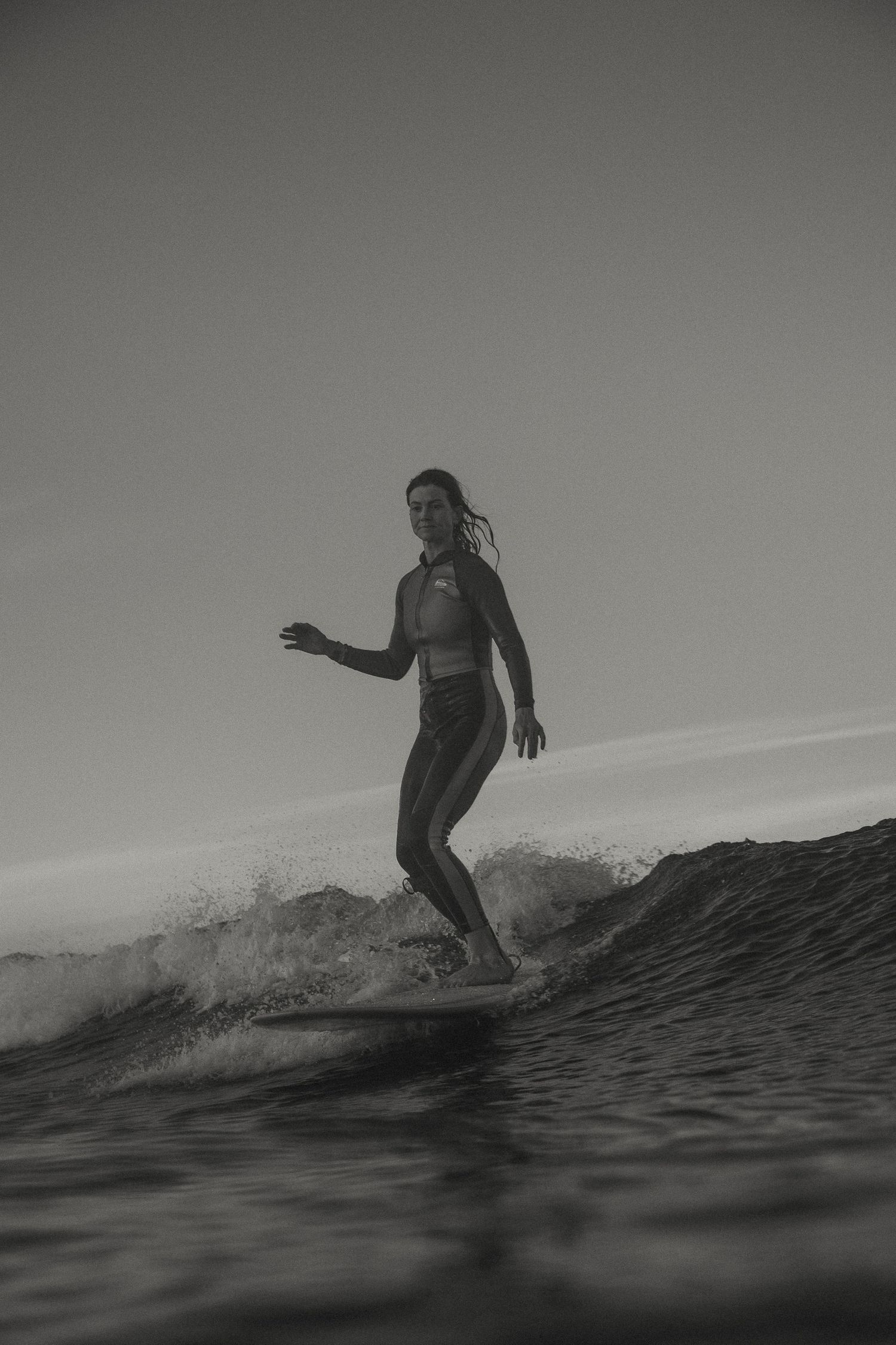 A surfer rides a breaking wave in dramatic black and white photography.