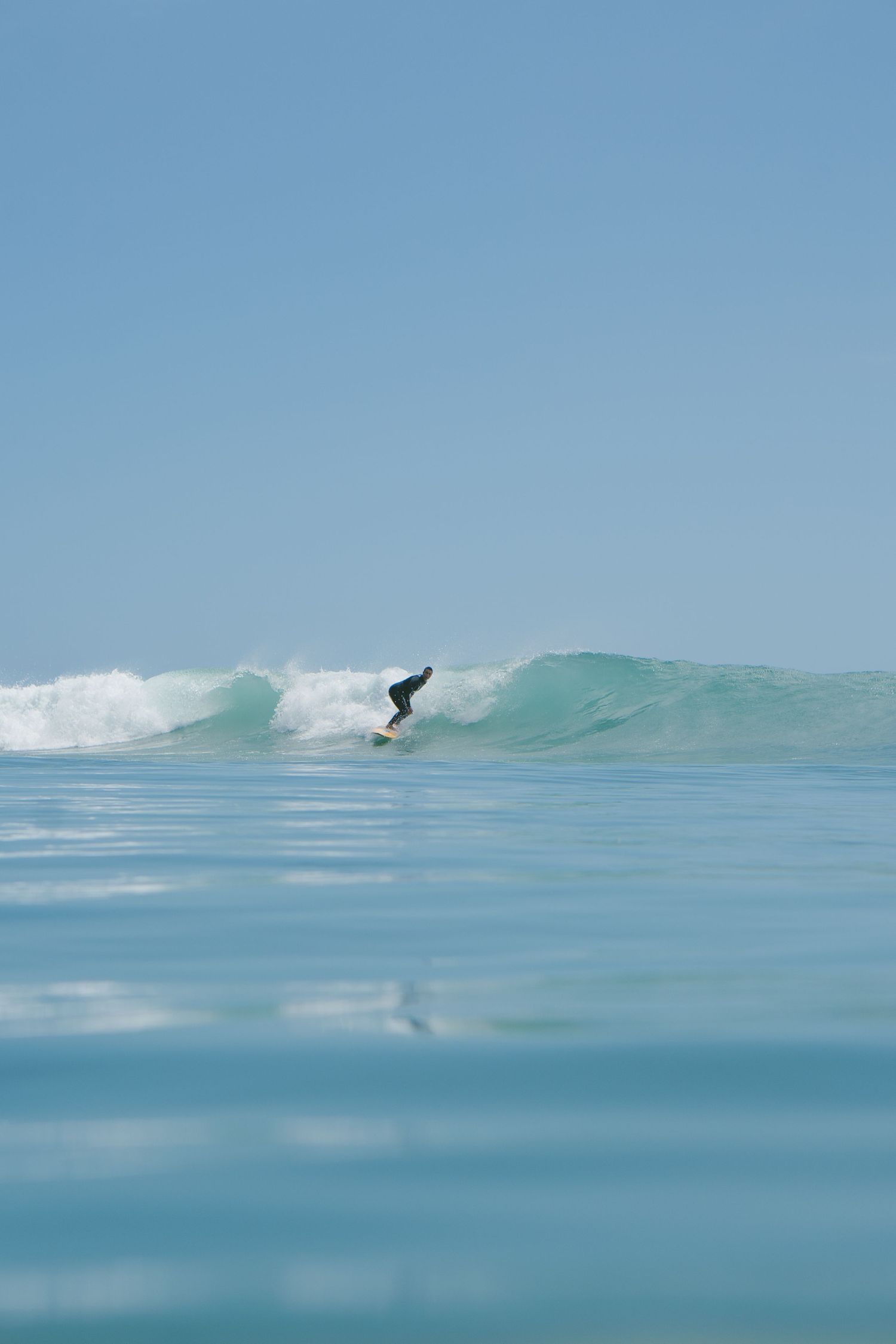 Silhouette of surfer catching a perfect turquoise wave on a clear sunny day.