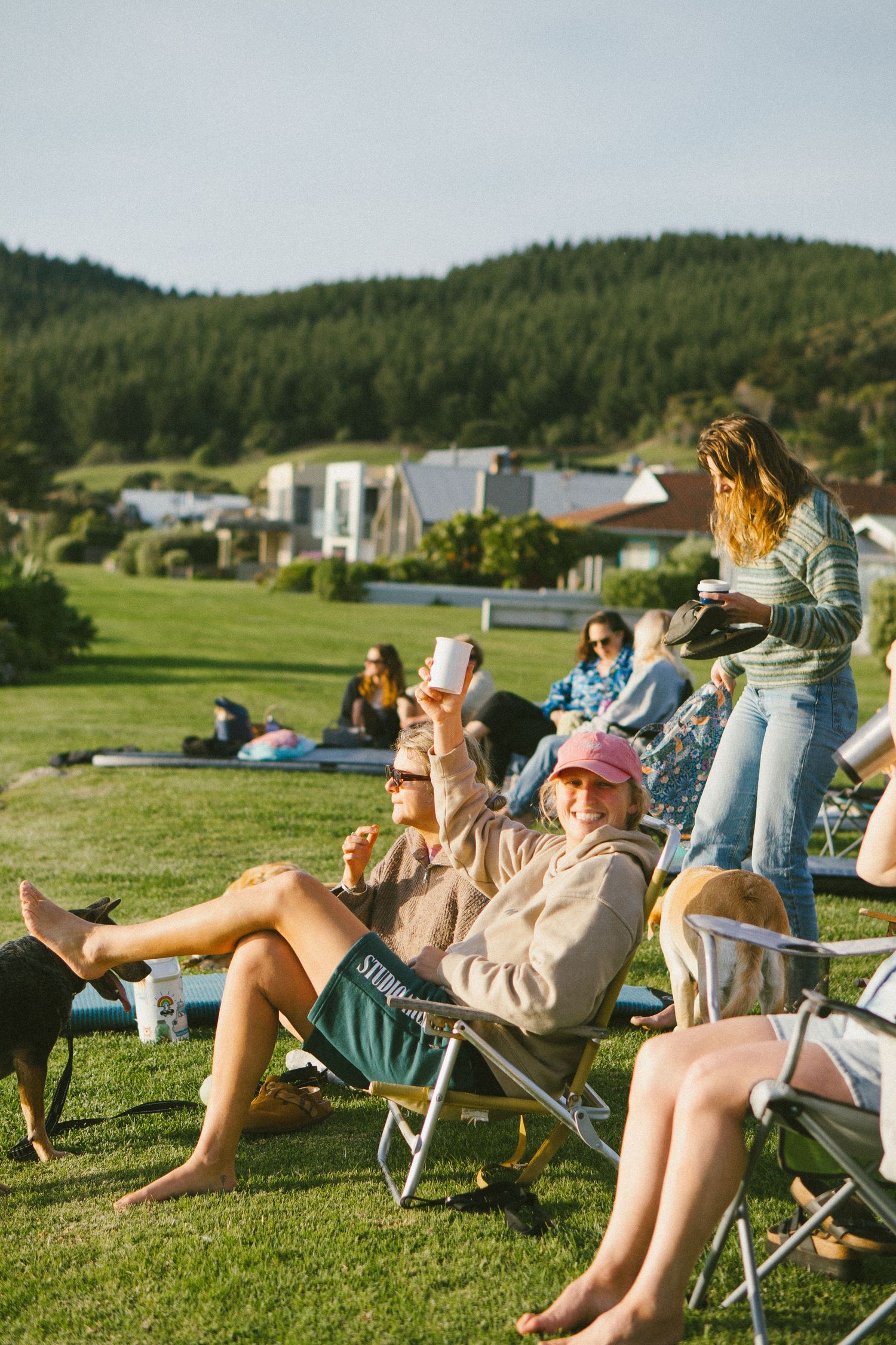 Group relaxing on lawn chairs at outdoor gathering with green hills in background.