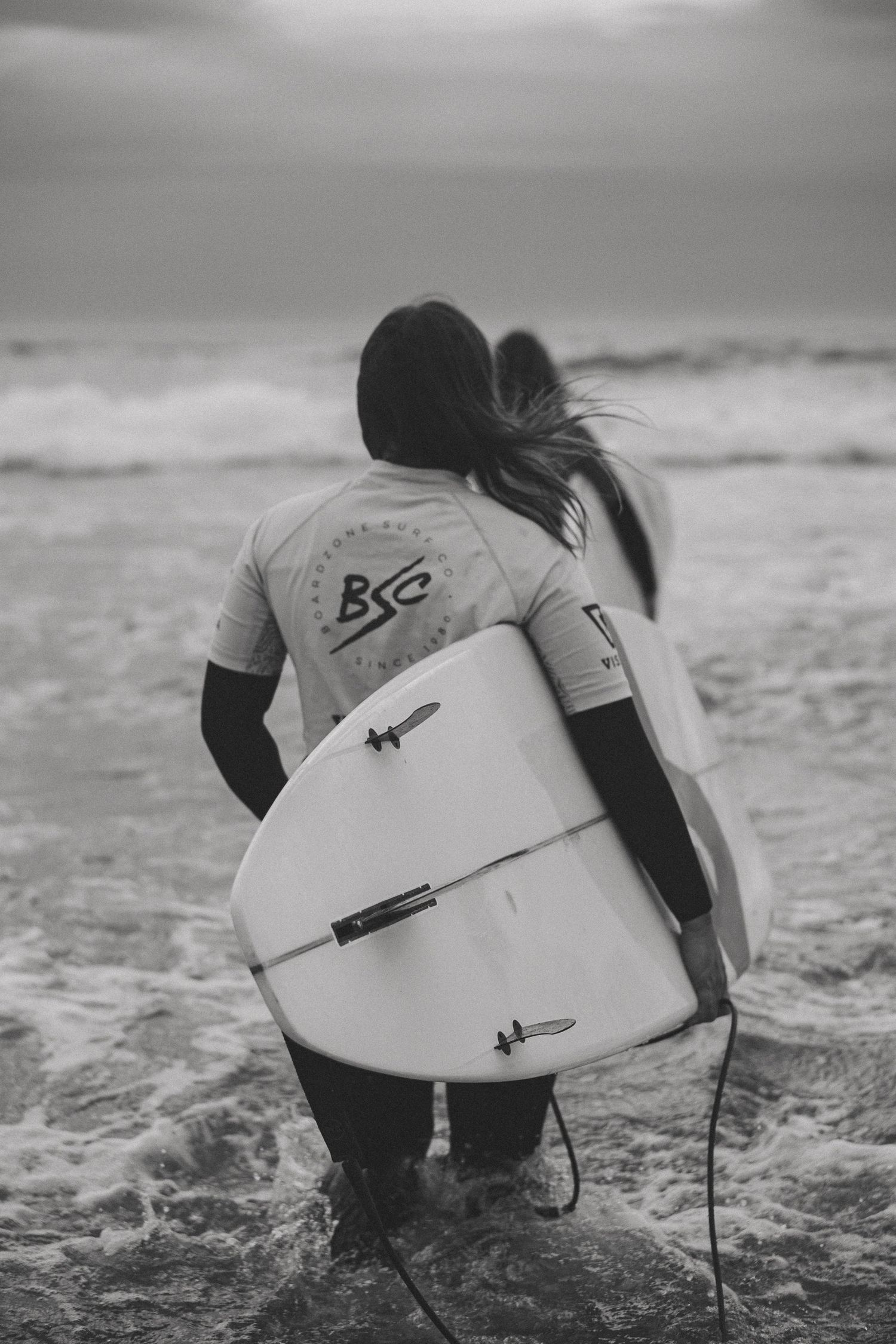 Black and white image of surfers wading into ocean water with surfboards.