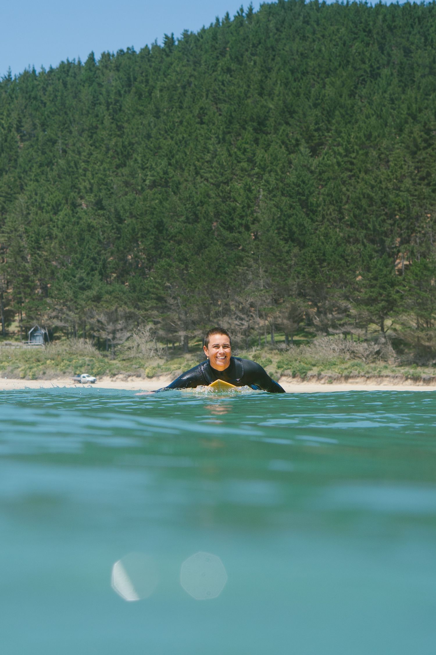 A swimmer floats in turquoise waters near a forested coastline.