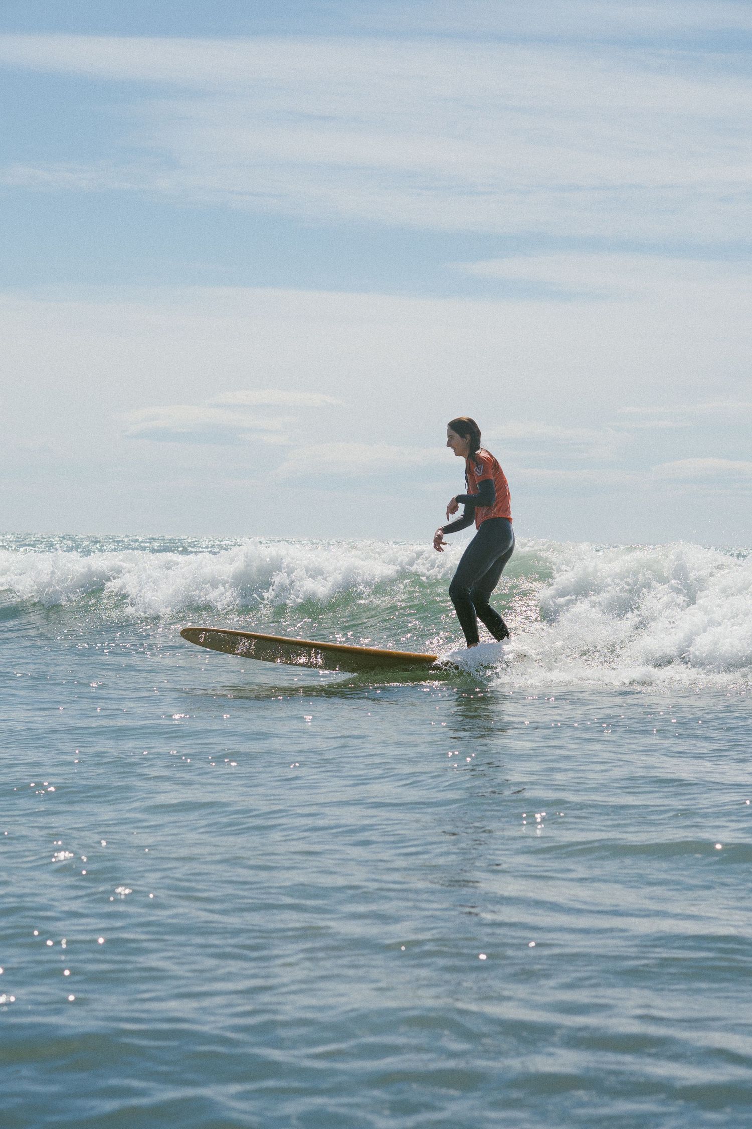 Surfer rides longboard across breaking wave on sunny day at sea.