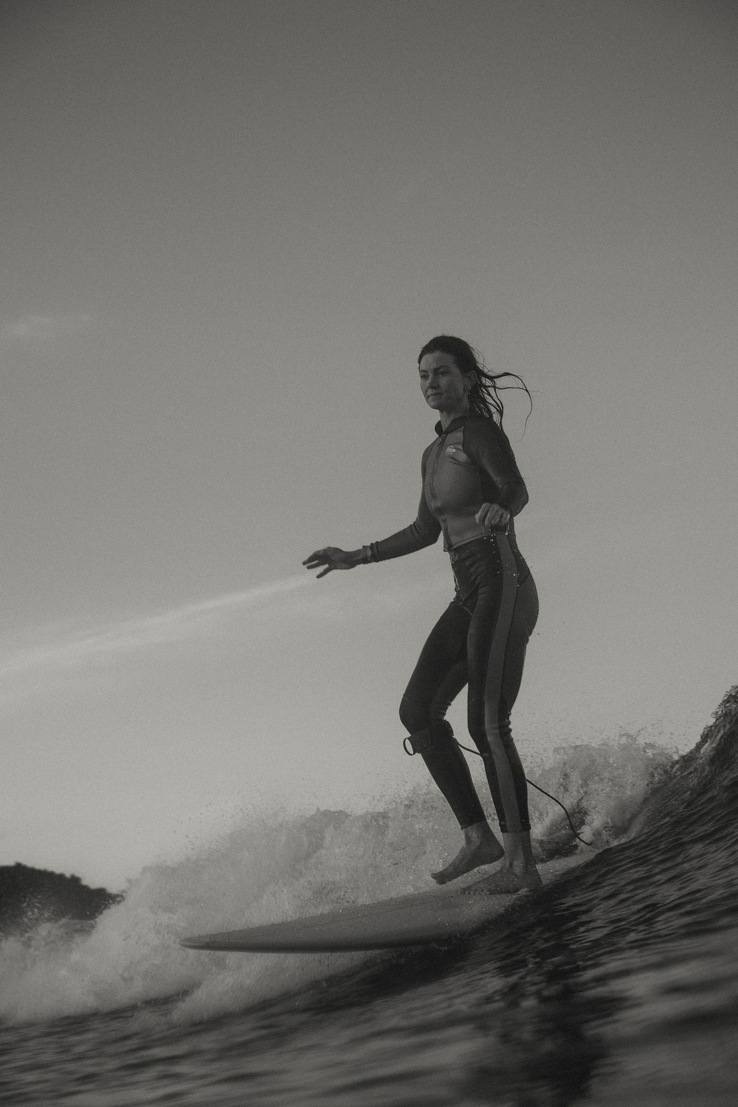 Black and white shot of surfer riding wave with dramatic water spray.
