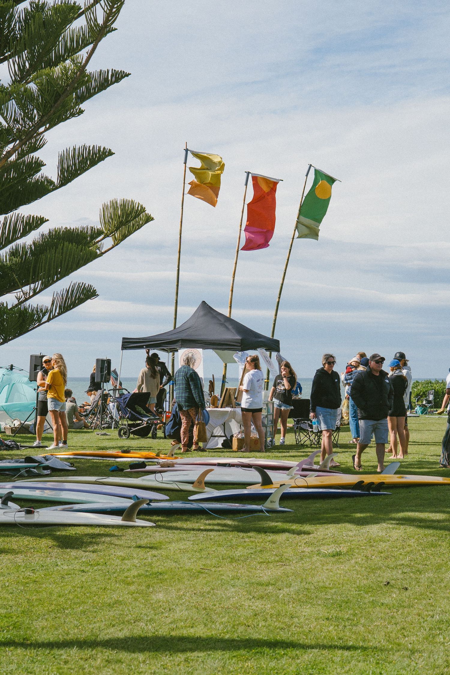 Surfing event with colorful flags and surfboards laid out on grass.