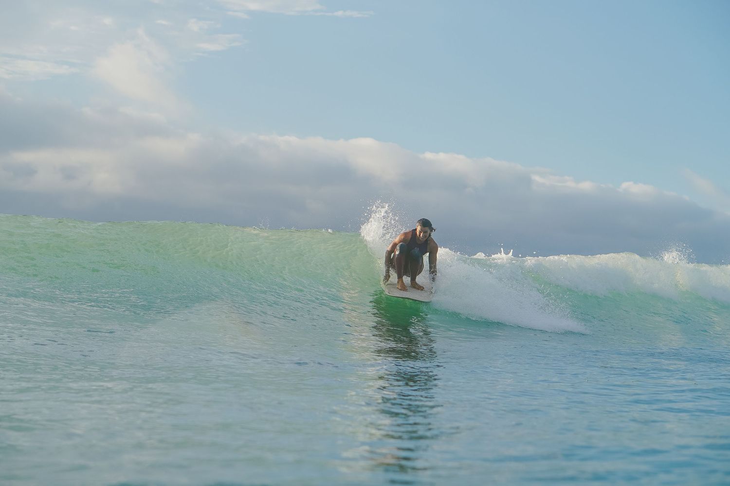 Surfer catches a clean wave in turquoise waters on a bright sunny day.