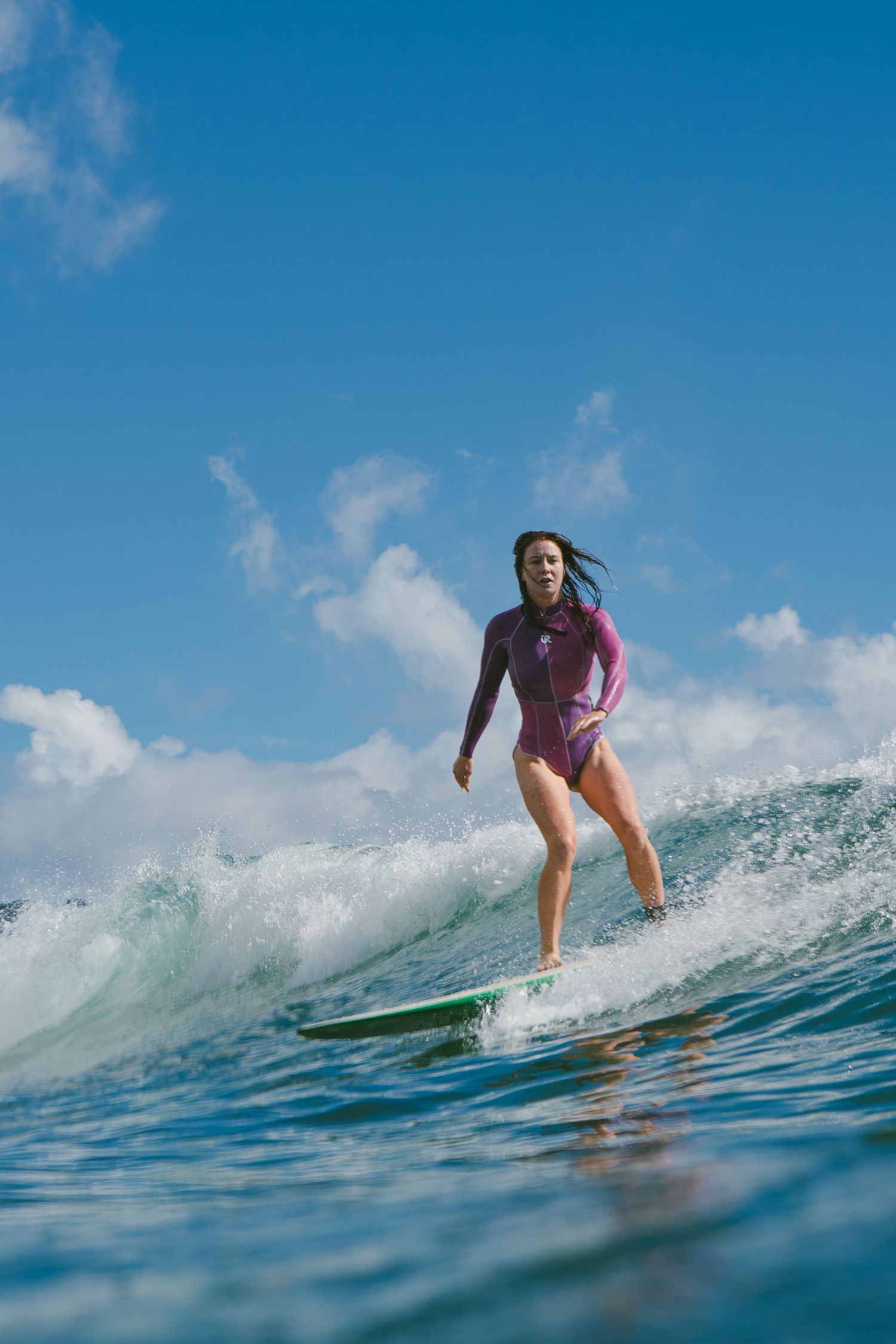 Skilled surfer navigates turquoise wave in purple wetsuit.
