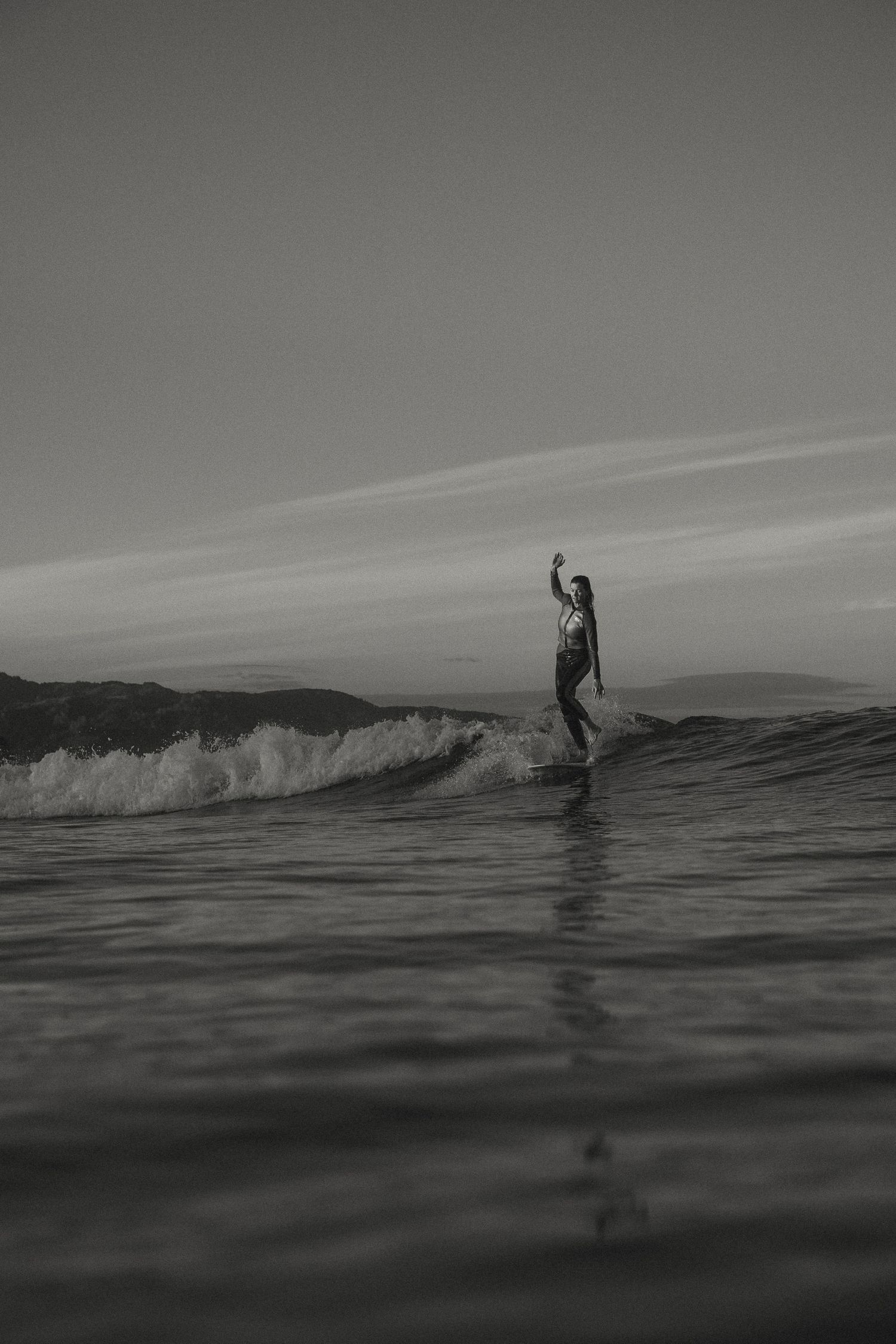 Silhouettes of surfers riding waves against a dramatic ocean horizon at dusk.