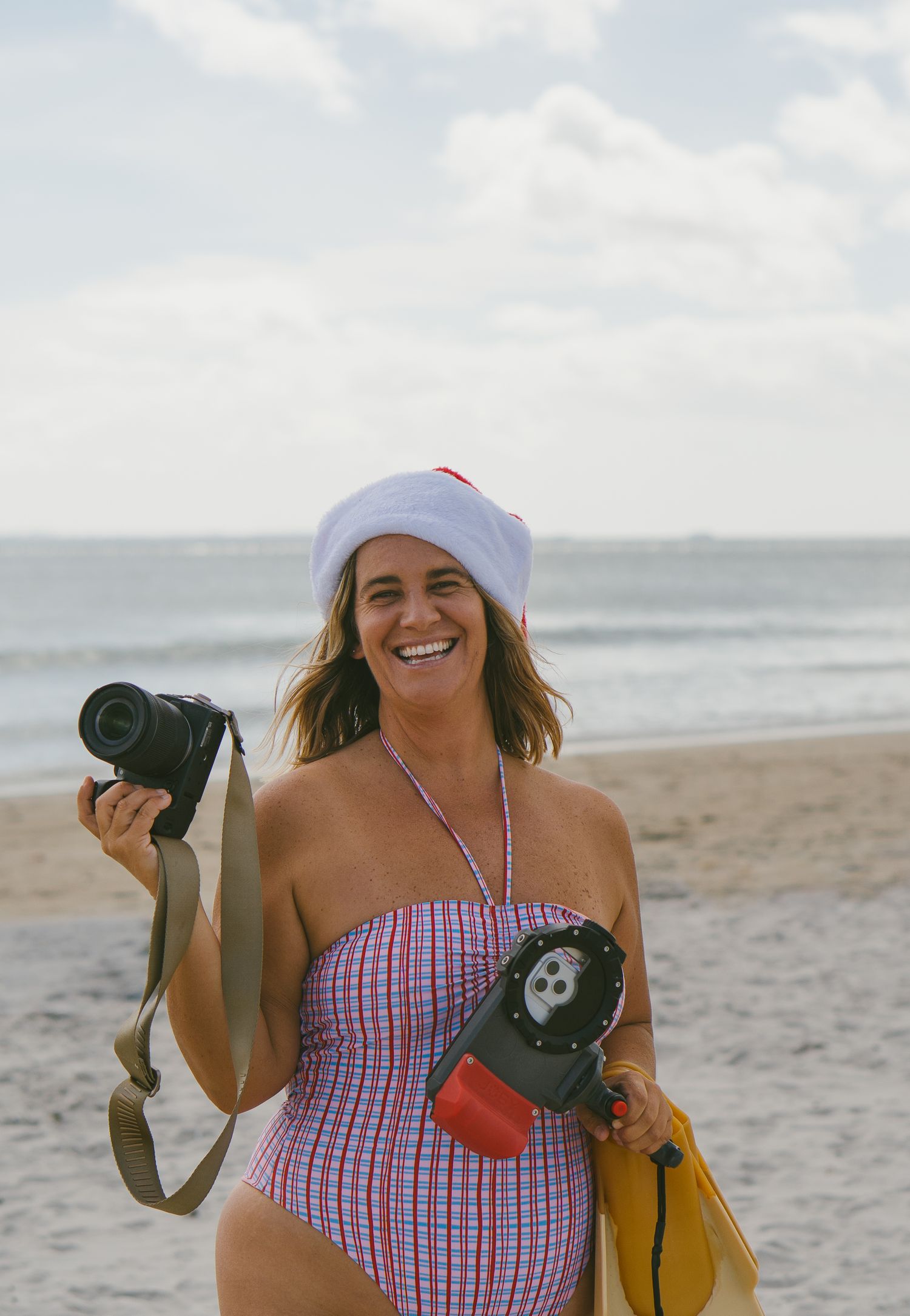 Person in red and white swimwear holding camera equipment on beach.