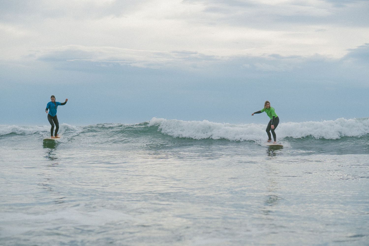 Multiple surfers riding waves in the ocean on a cloudy day.